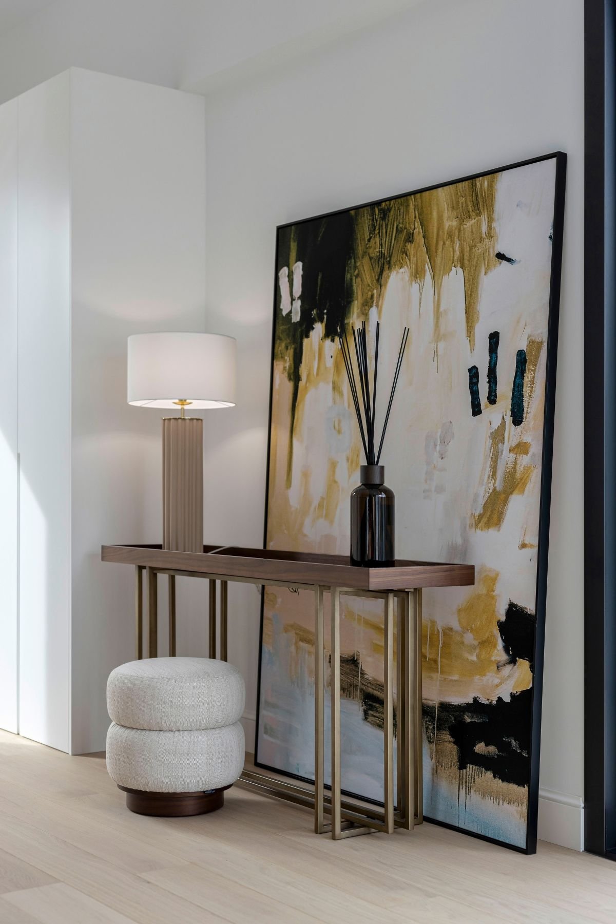 Perspetiva de consola entrada com candeeiro de mesa e quadro artístico de grande formato, ideal para um hall de entrada pequeno assinado com sublime interior design.