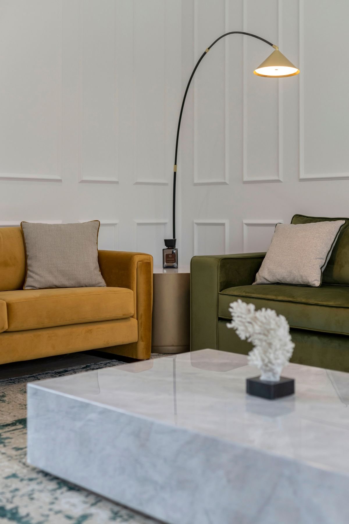 Sofá em veludo mostarda e poltrona para sala verde com candeeiro de pé e mesa de centro em mármore, compondo uma sala de estar moderna com elegantes moveis sala tv modernos.