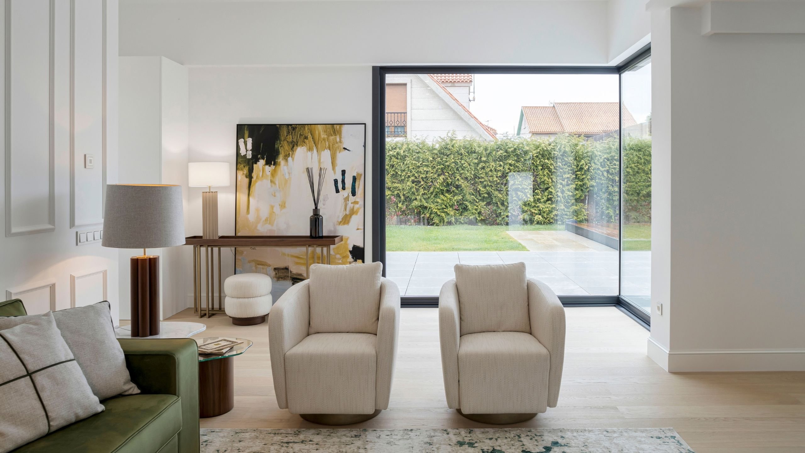 Dupla poltrona para sala redonda voltada para o jardim envidraçado junto a sofá verde e consola, realçando uma sala de estar moderna com moveis sala tv modernos.