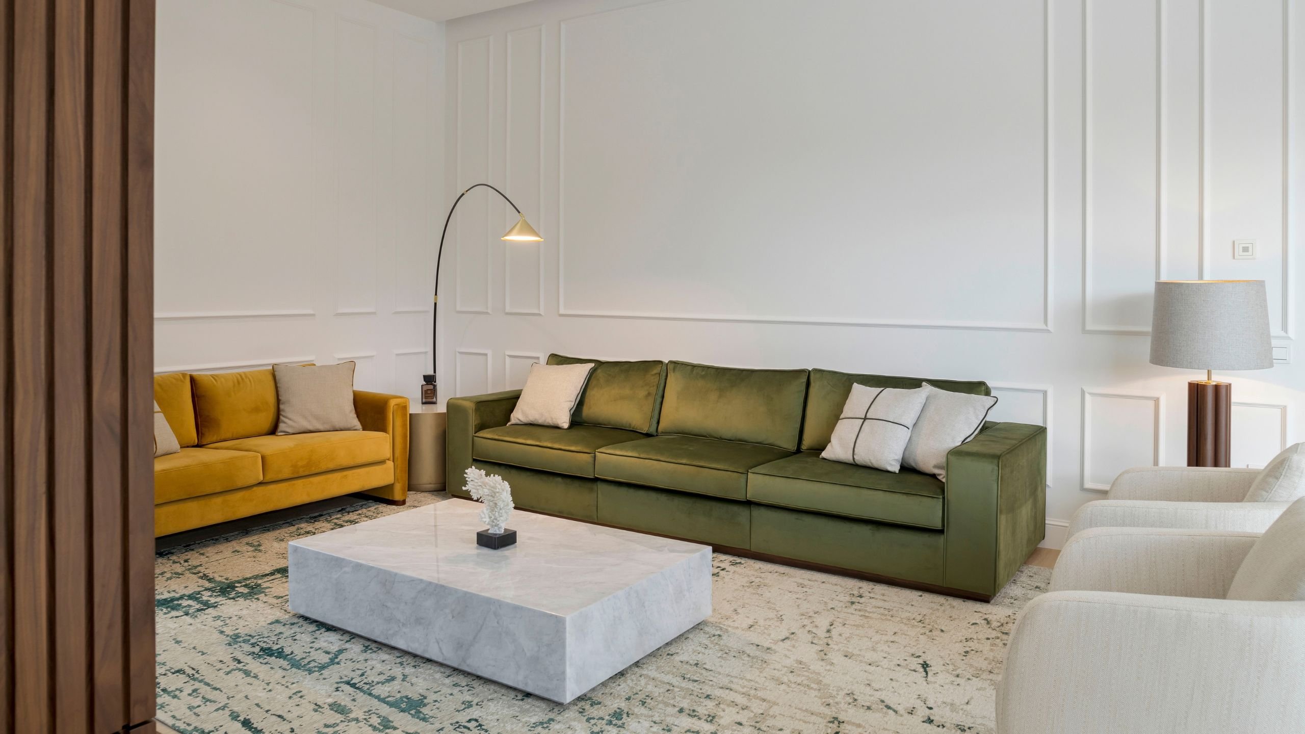 Ampla sala de estar moderna com sofá verde aveludado, sofá mostarda, poltrona para sala clara e mesa de centro em bloco marmoreado em harmonia com moveis sala tv modernos.