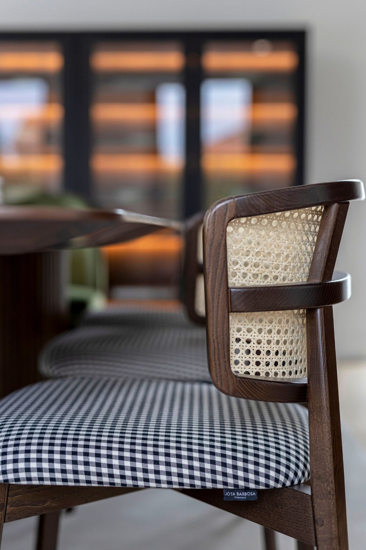 Pormenor de cadeira sala de jantar em madeira escura com palhinha e padrão vichy junto a mesa para sala de jantar, numa requintada sala de jantar em open space.
