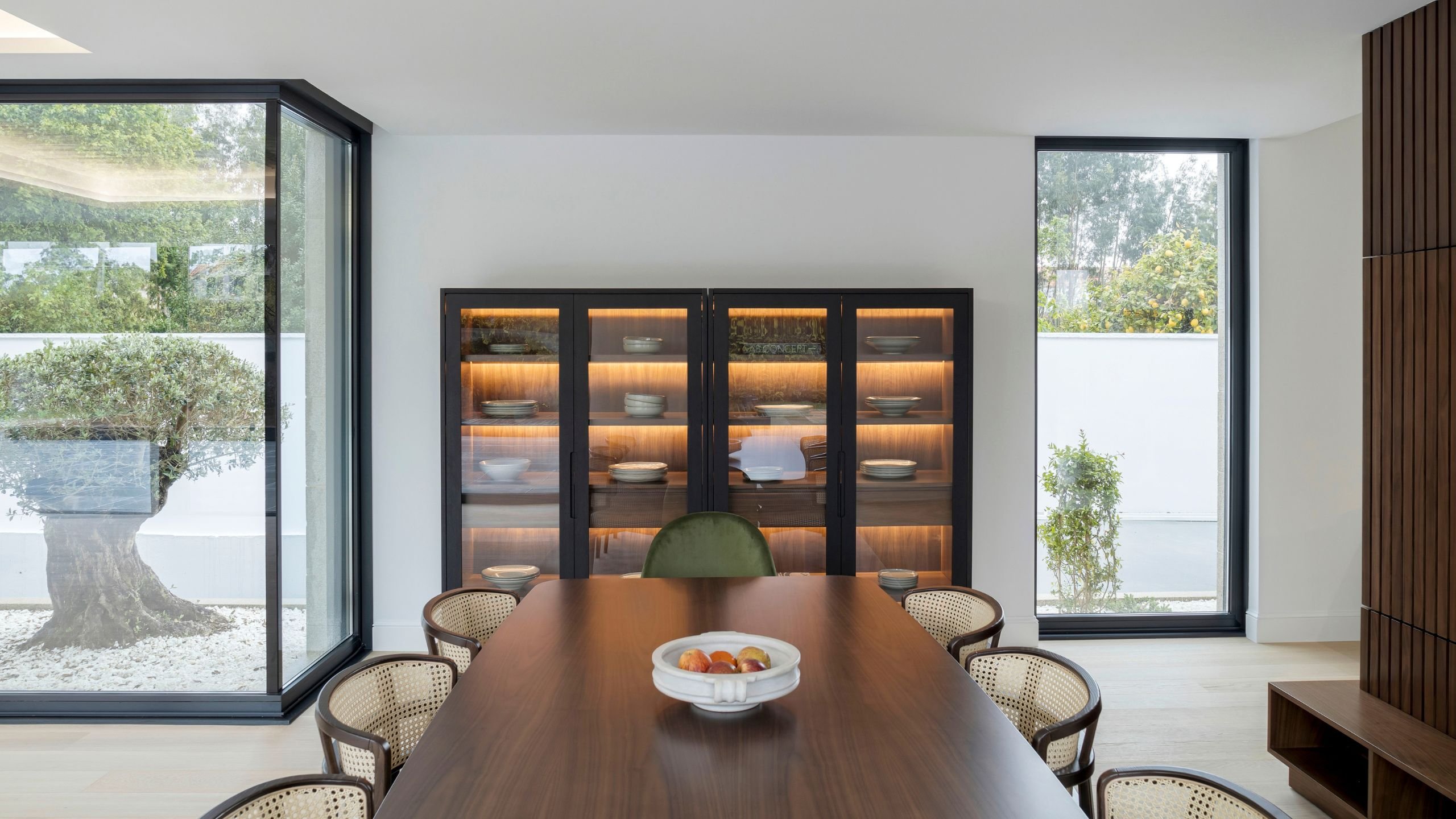 Vista de mesa para sala de jantar e cadeira sala de jantar com costas em palhinha diante de louceiro iluminado, integrando a sala de jantar em open space.