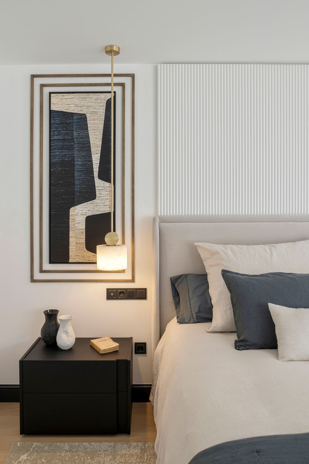 Pormenor de cama de casal com cabeceira canelada e mesa de cabeceira preta de linhas retas na decoração de quarto.