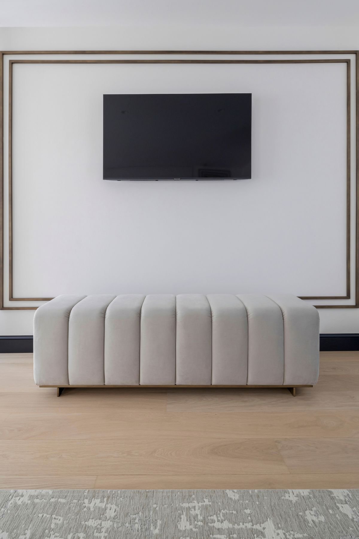 Banco estofado canelado sob televisão em parede com molduras elegantes na decoração de quarto.