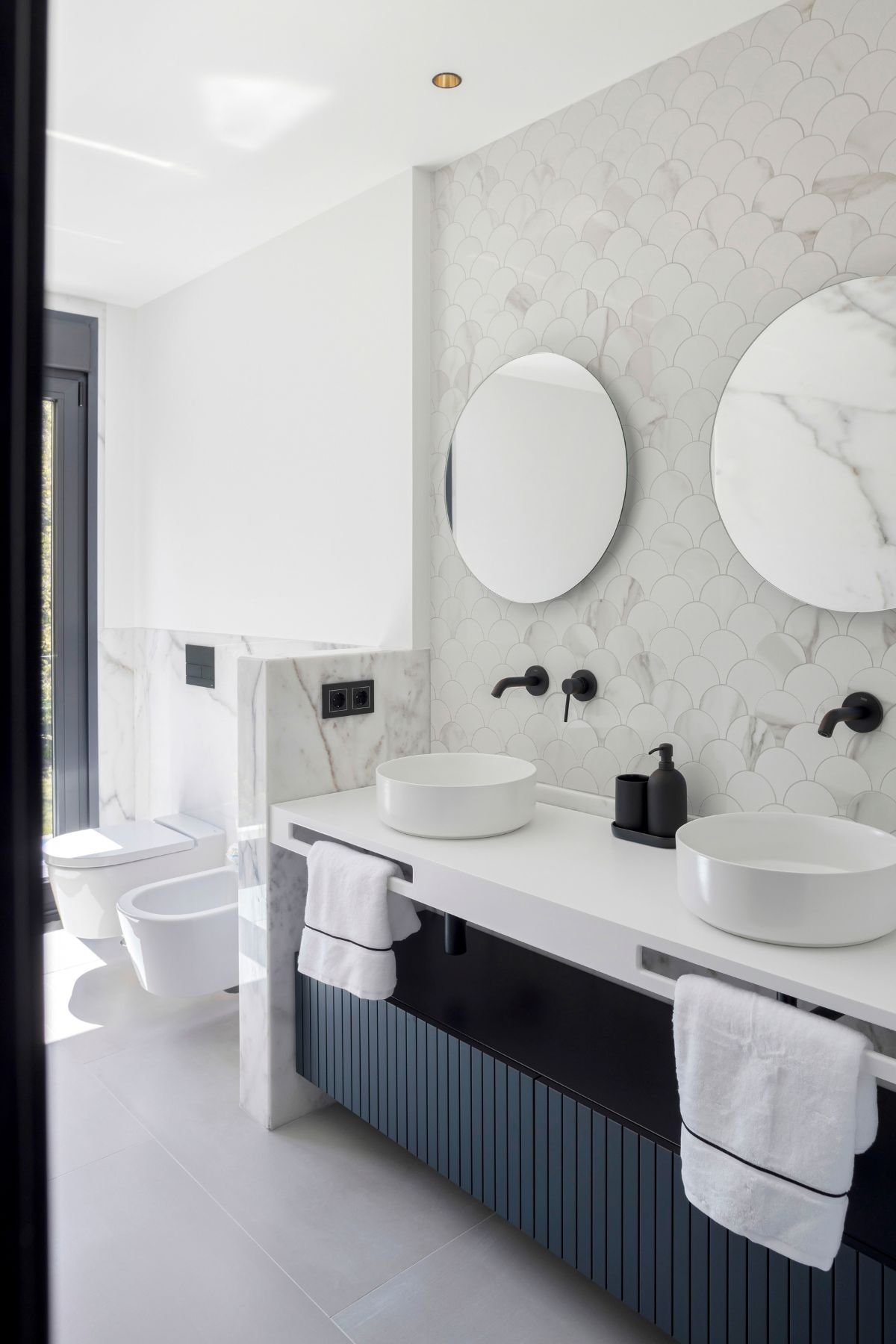 Lavatórios duplos sobre armário casa de banho ripado escuro com espelhos redondos, exemplo de casas de banho modernas com elegante interior design.