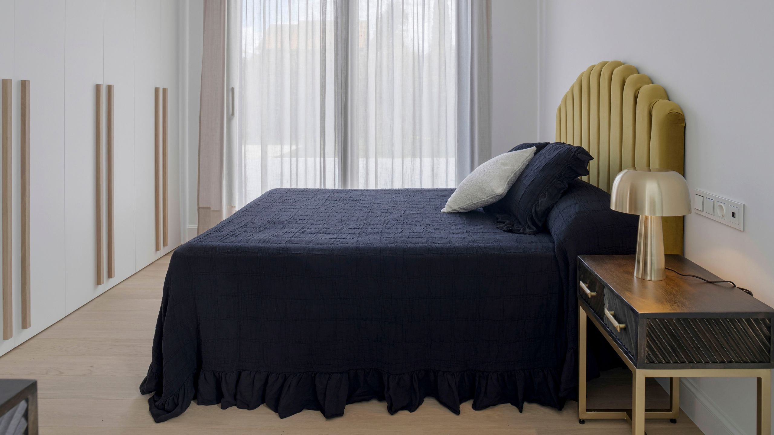 Cama de casal com roupa de cama preta e mesa de apoio ao lado de roupeiros embutidos, exemplo de harmonia em design de interiores.