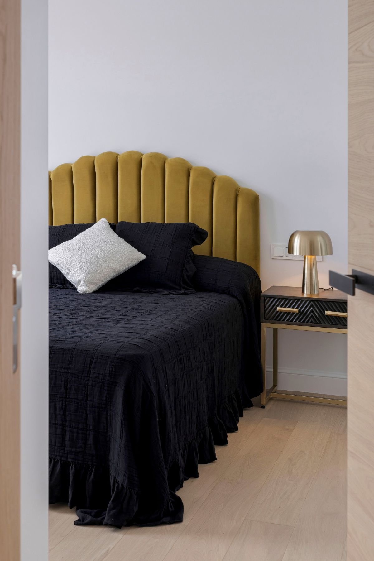 Pormenor de cama de casal com cabeceira canelada em veludo amarelo e candeeiro dourado, evidenciando o design de interiores.