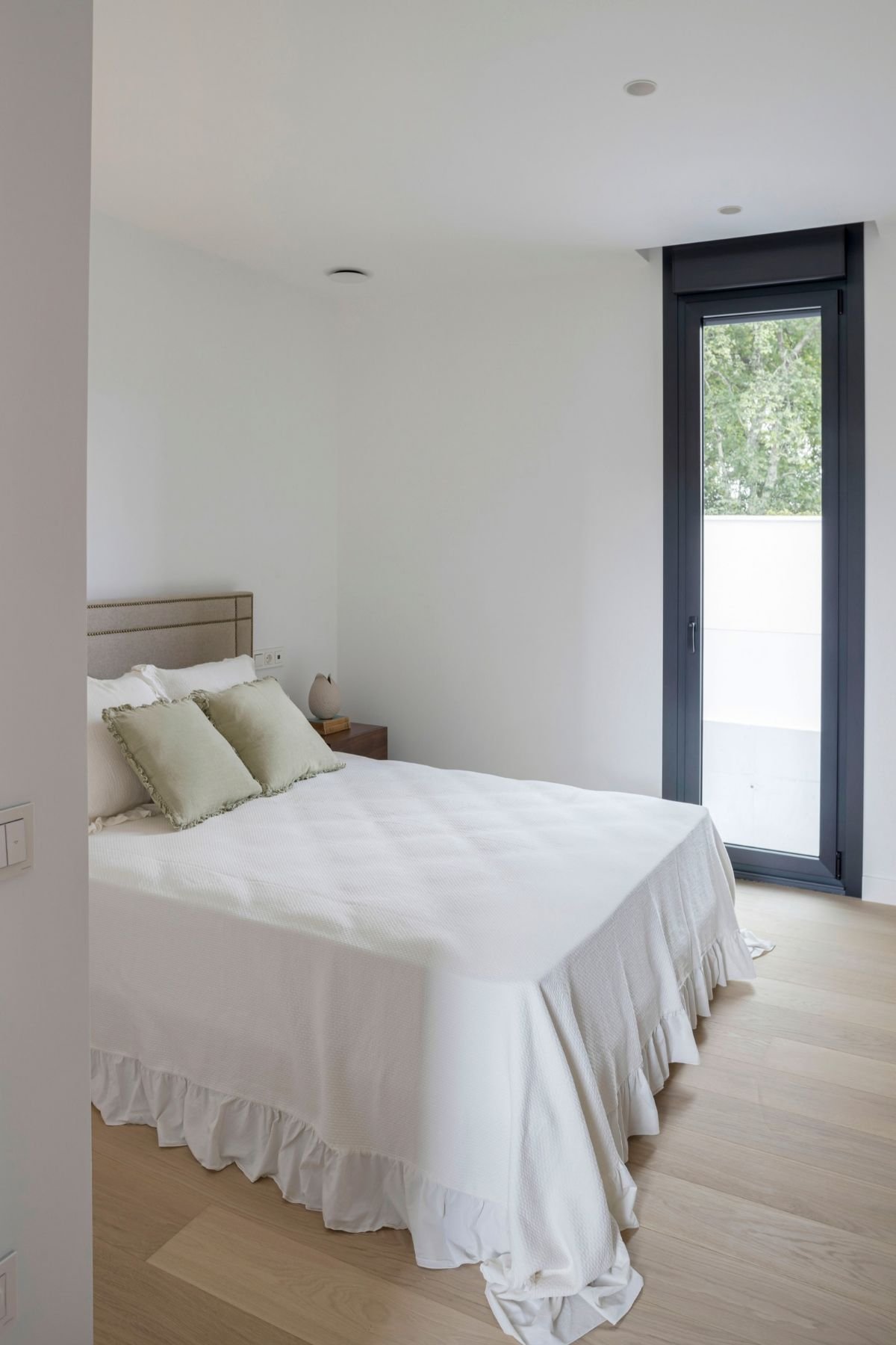 Quarto de hóspedes luminoso com janela ampla e cama de casal de tons claros, exemplo de excelência em design de interiores aplicada à decoração de quarto.