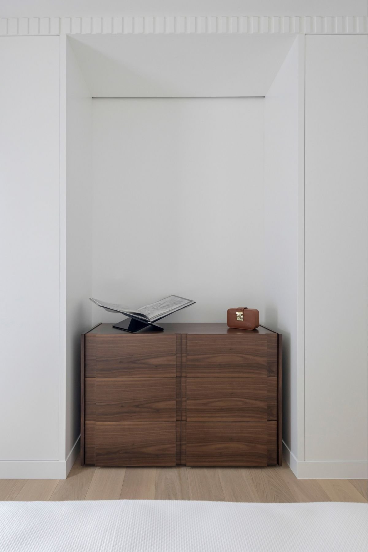 Cómoda de linhas direitas em nicho de parede sob iluminação discreta em quarto de hóspedes, integrando o design de interiores e uma serena decoração de quarto.