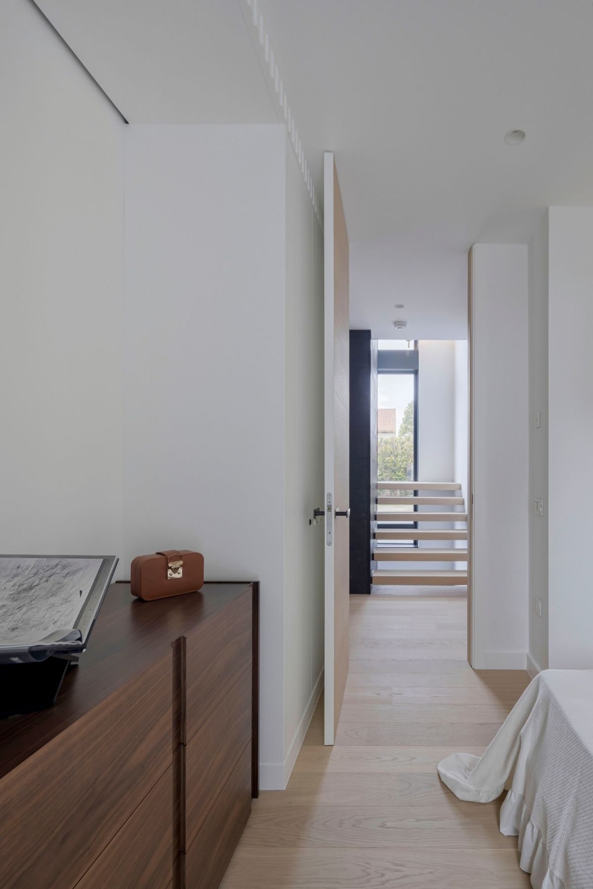 Perspetiva da porta para o quarto de hóspedes com cómoda em nogueira e vista para as escadas, unindo design de interiores a uma harmoniosa decoração de quarto.
