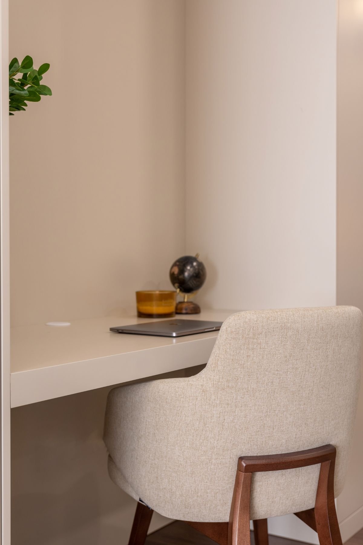 Detalhe do canto do escritório minimalista com computador portátil, jarra decorativa e globo sobre a bancada beige.