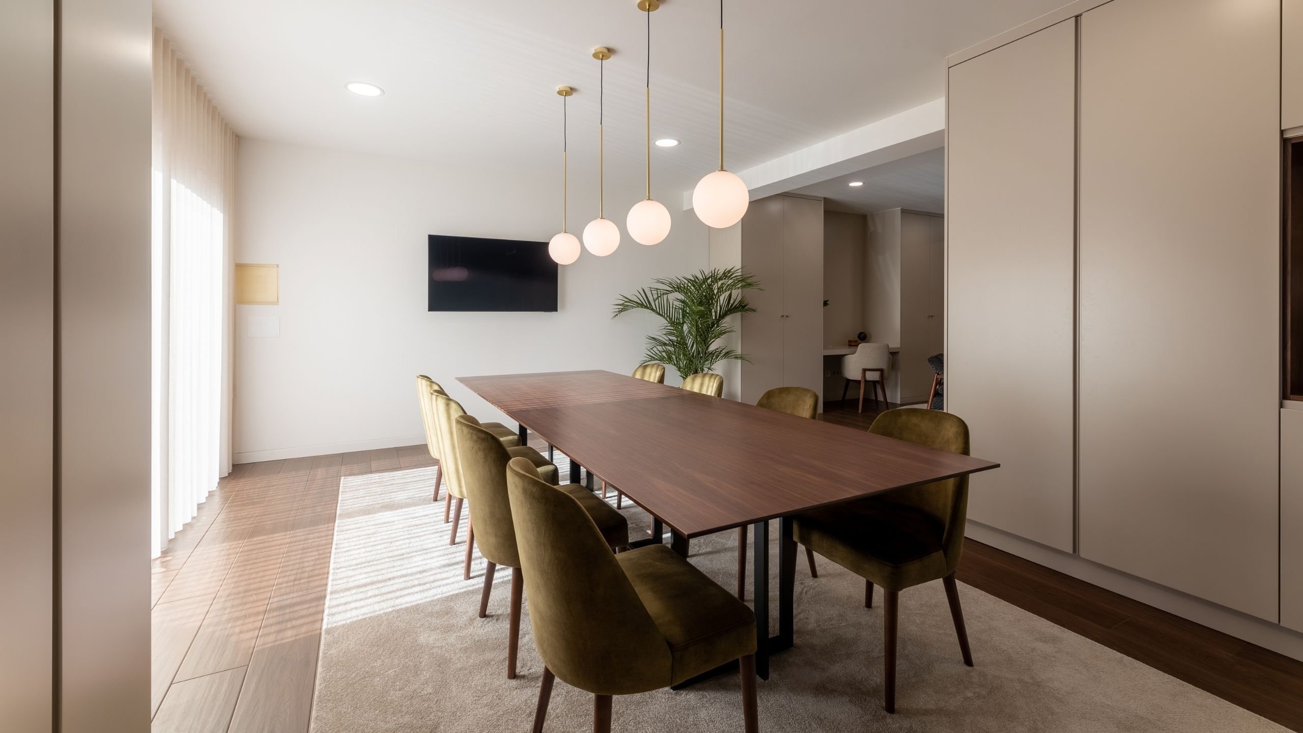 Vista em perspetiva da sala de jantar contemporânea iluminada por luz natural vinda da grande janela lateral.