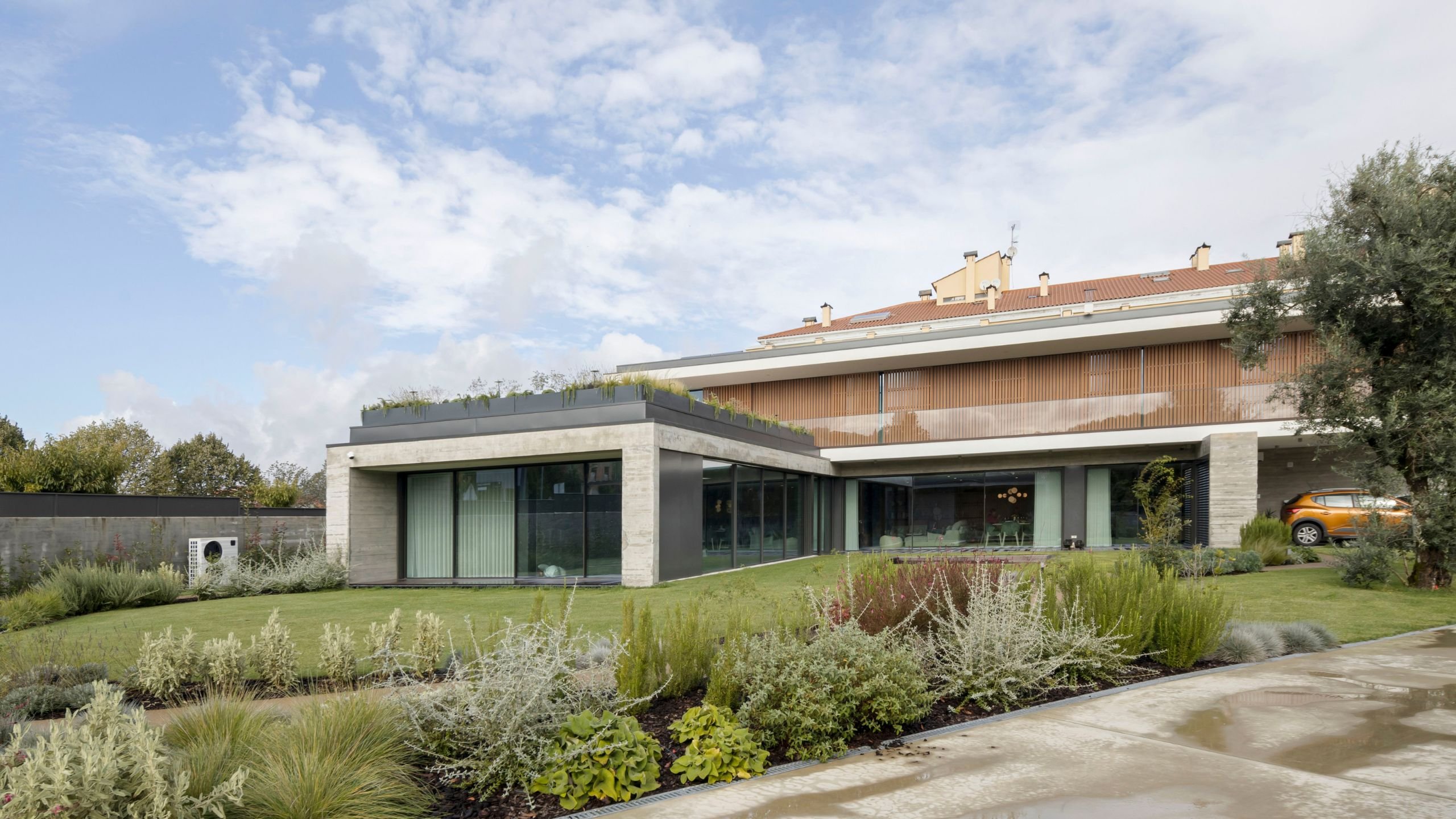 Exterior de moradia moderna em Viseu com fachada em betão e madeira, amplas superfícies vidradas, jardim relvado bem cuidado e cobertura vegetal.