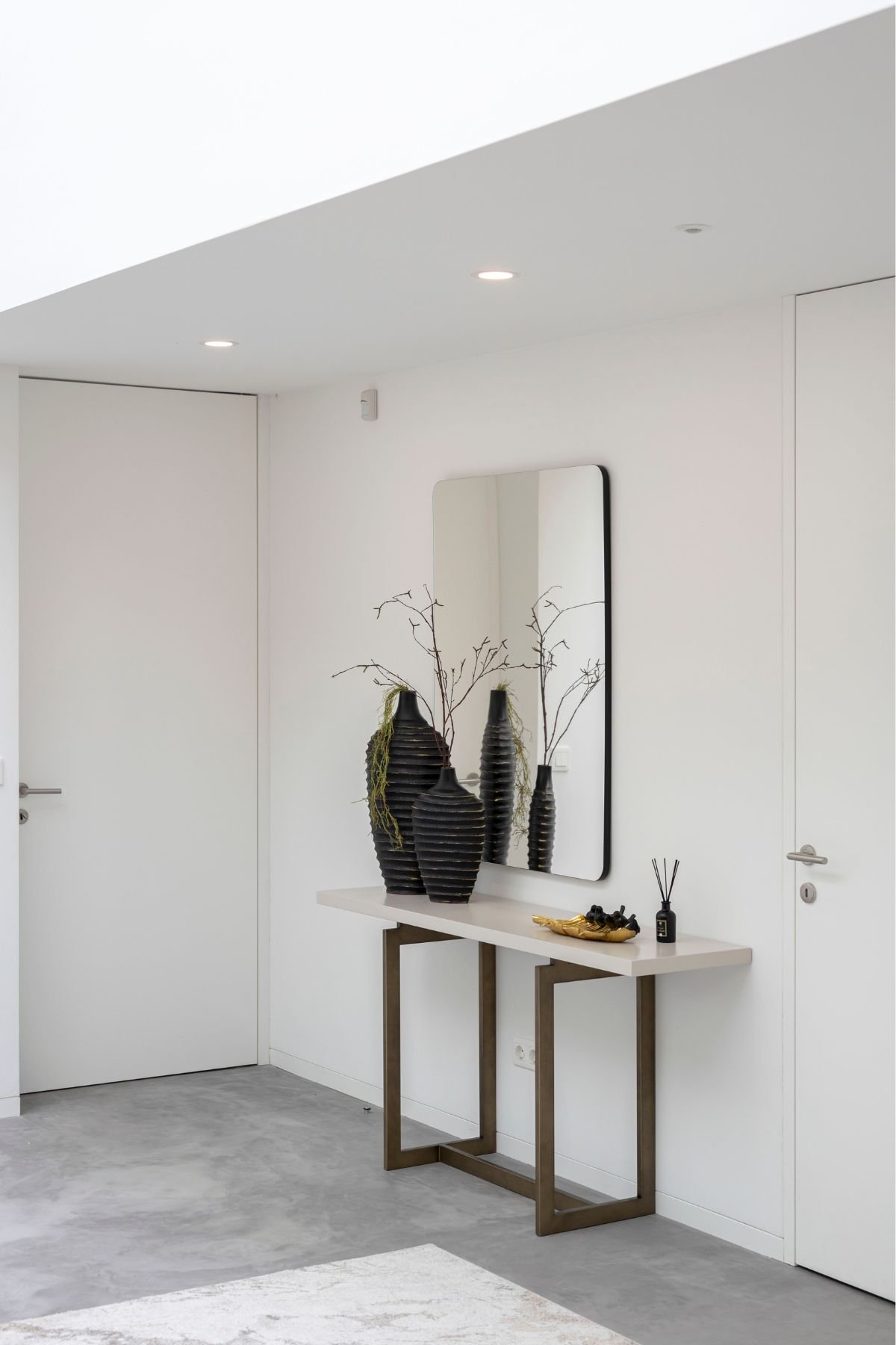 Hall de entrada minimalista com piso em microcimento, consola de design em tom claro, espelho retangular e portas brancas de linhas simples.