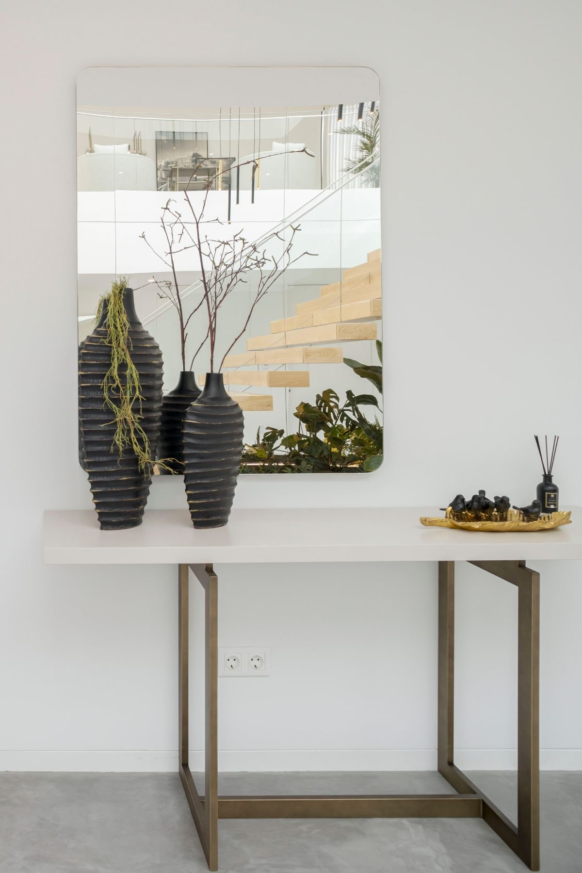 Espelho personalizado a refletir a luz natural e a escada flutuante de madeira, sobre consola contemporânea no hall de entrada.