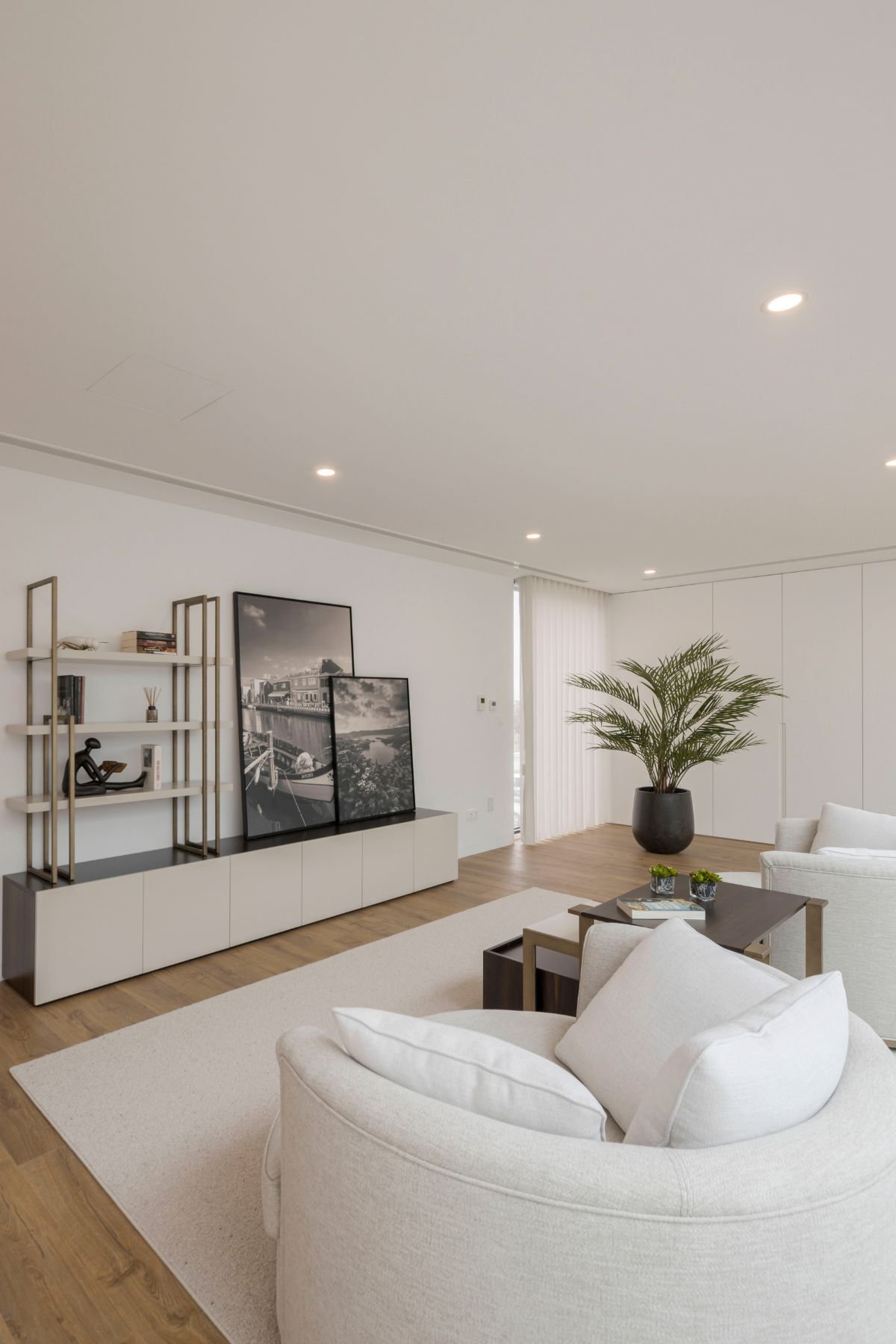 Sala de leitura no Mezzanine com cadeirões em tom creme, tapete neutro, estante em estrutura metálica com livros, quadros em preto e branco e planta em vaso escuro.