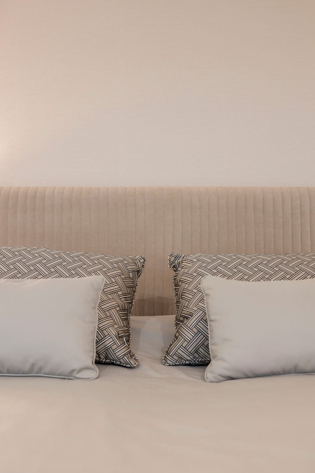 Detalhe da cabeceira da cama em veludo canelado bege com almofadas decorativas em padrão geométrico e tons neutros.