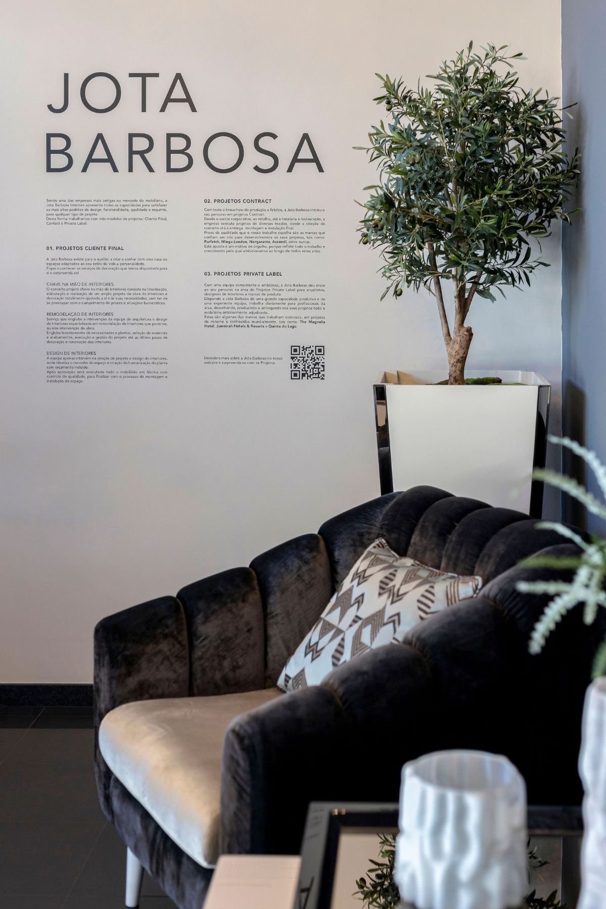 Parede do hall de entrada moderno com o logótipo da marca, acompanhada por um sofá de veludo e uma planta decorativa.