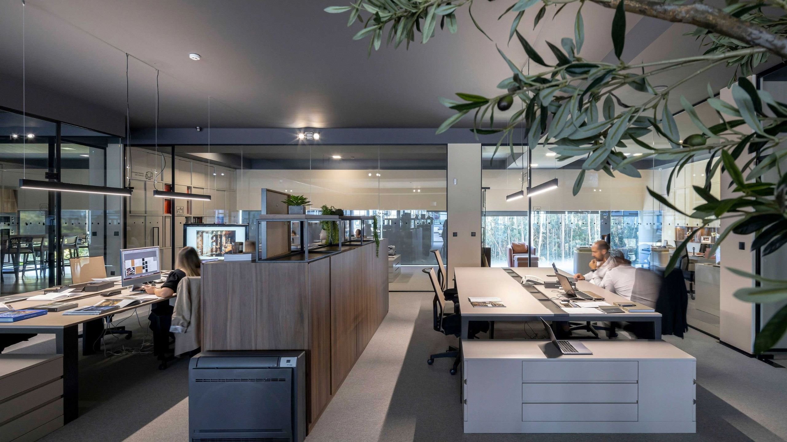 Ambiente de trabalho em open space com várias secretárias de escritório integradas e divisórias em vidro.