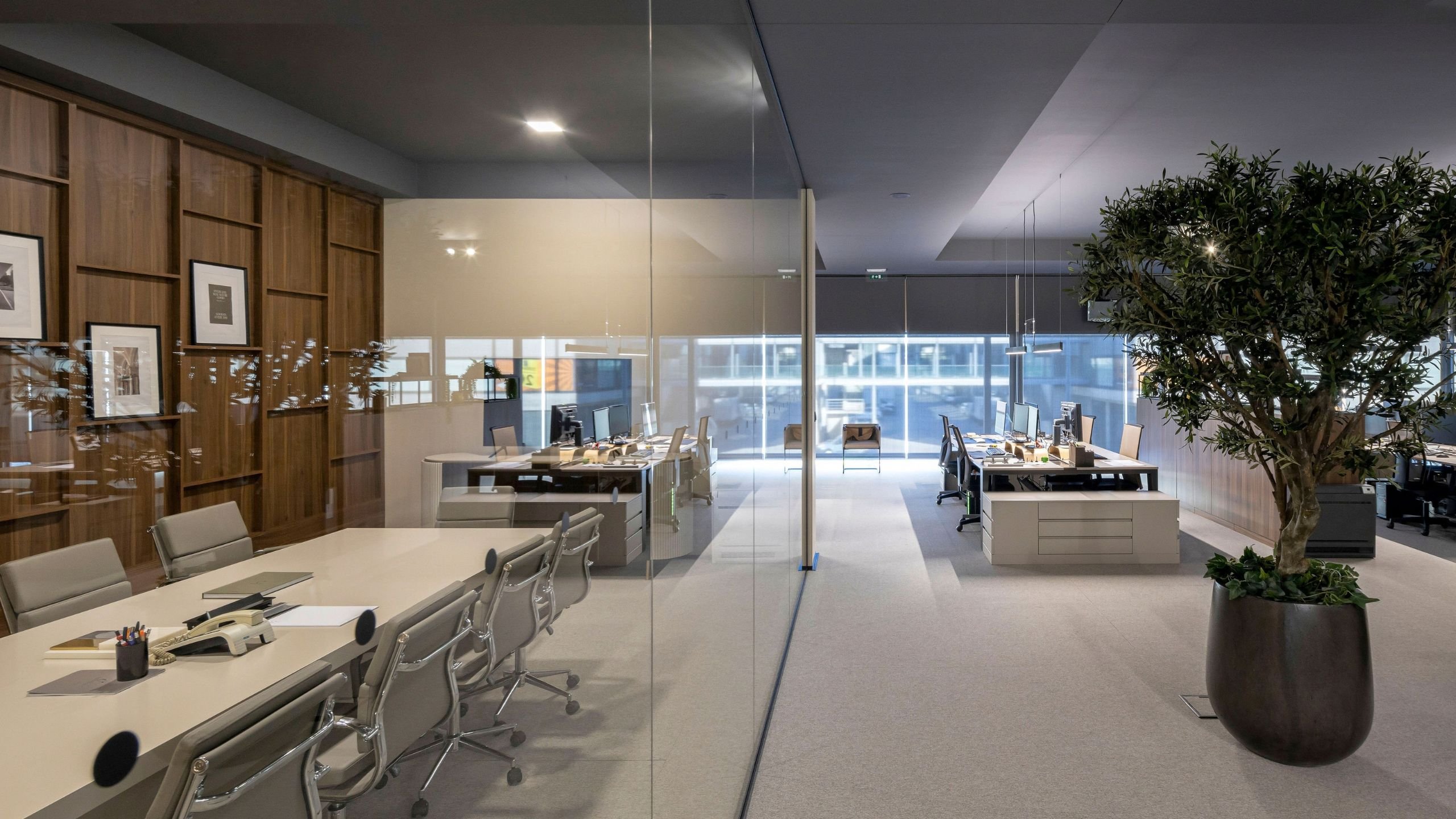 Transição visual entre o espaço privado e o open space corporativo com secretária de escritório.