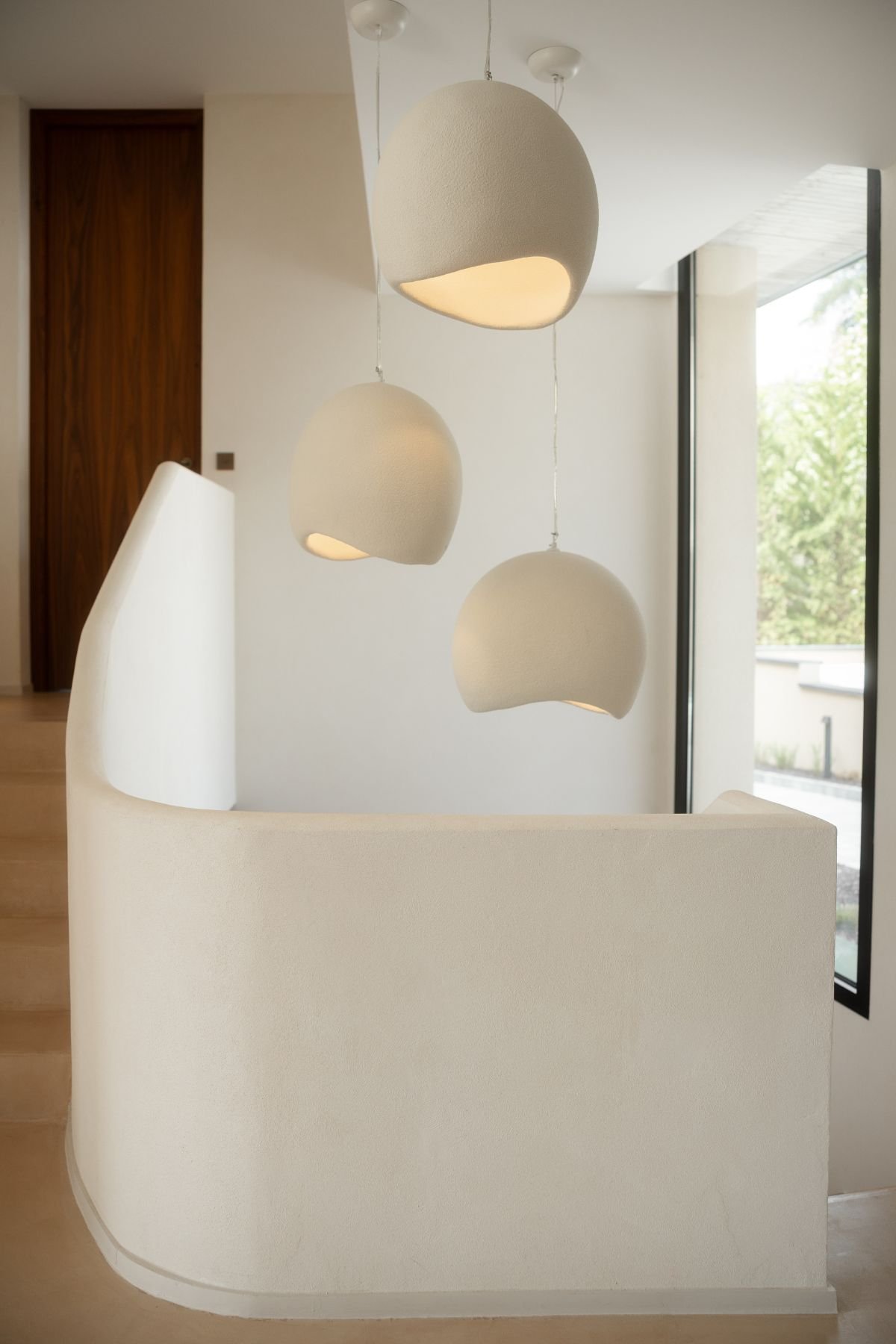Candeeiros de teto suspensos de design moderno a iluminar o vão de escadas interiores de tom claro.