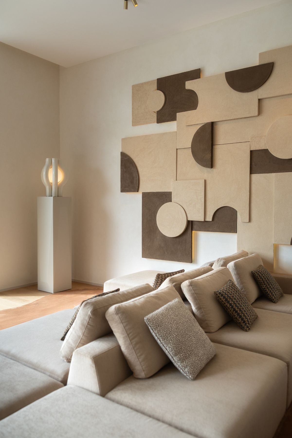 Pormenor das almofadas decorativas sobre o sofá e candeeiro de pé sobre pedestal junto a painel artístico.