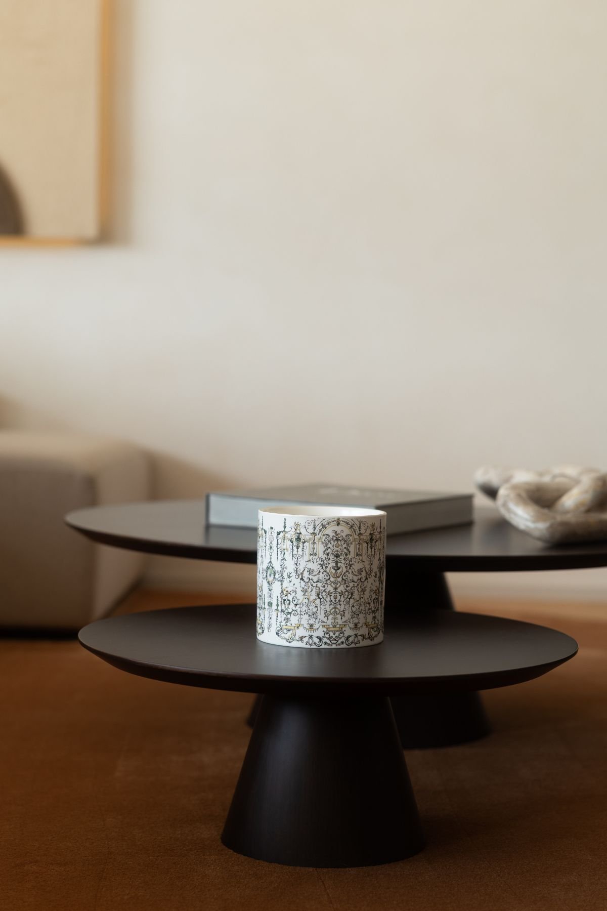 Pormenor das mesas de centro escuras na sala de estar com elemento decorativo e velas aromáticas sobre a bancada.