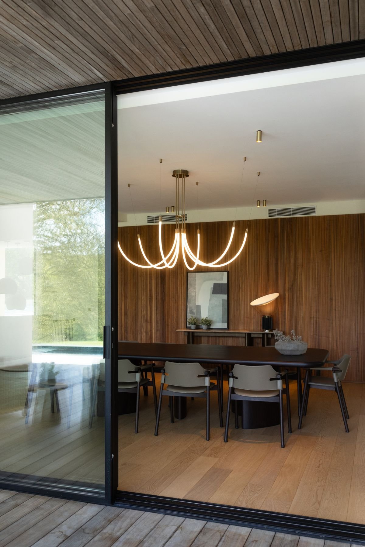 Sala de jantar vista do exterior com mesa para sala de jantar, candeeiro suspenso cénico e parede ripada.