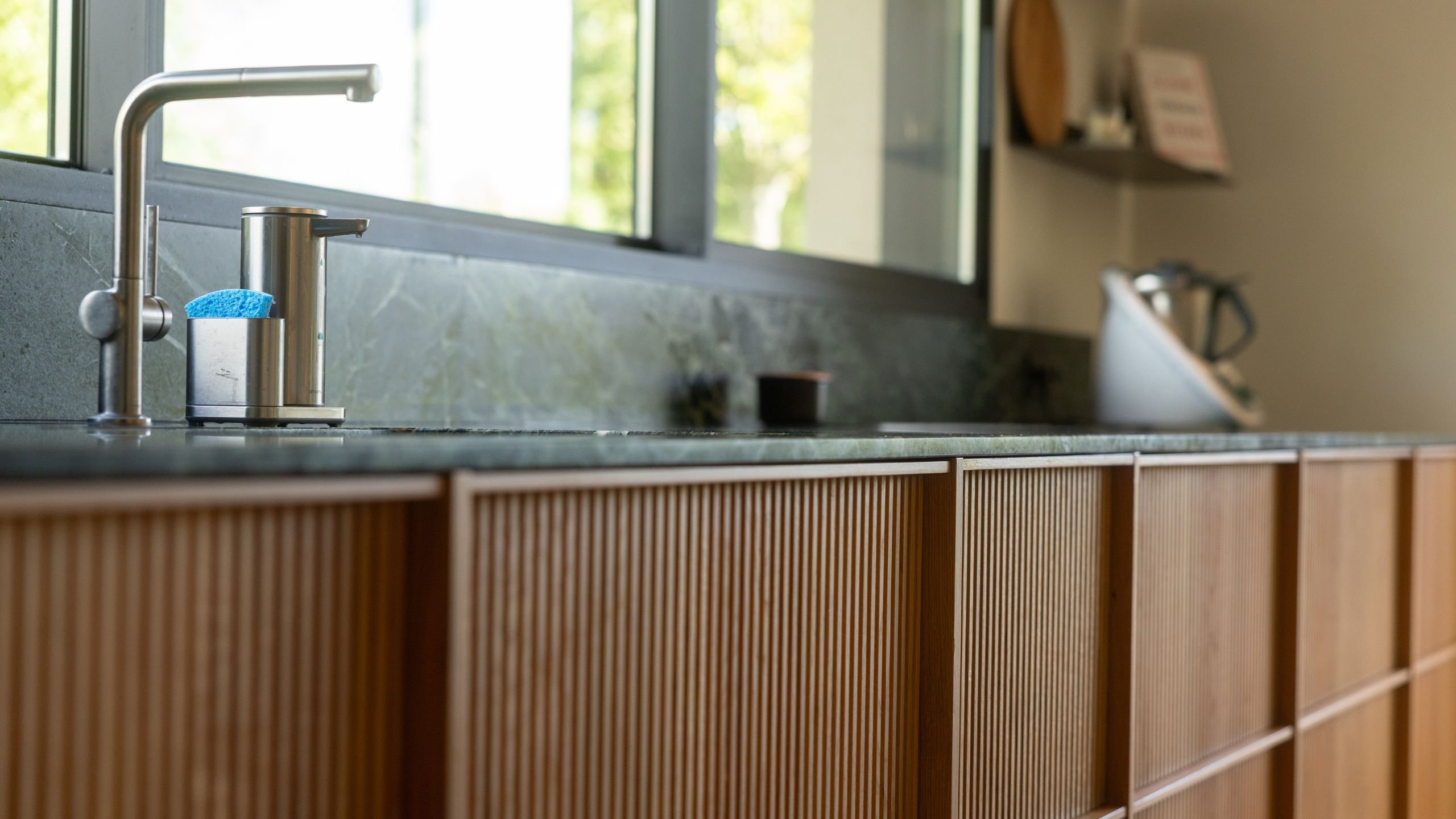 Bancada de cozinha moderna com bancada em mármore, armários em madeira ripada e torneira de encastre.