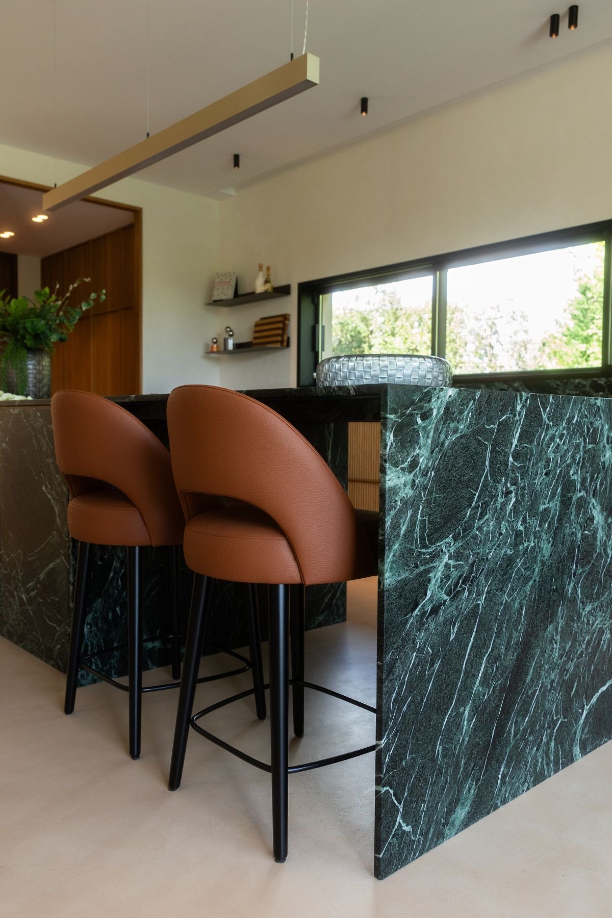 Ilha de cozinha moderna em mármore verde Guatemala acompanhada por dois bancos altos para cozinha em pele.