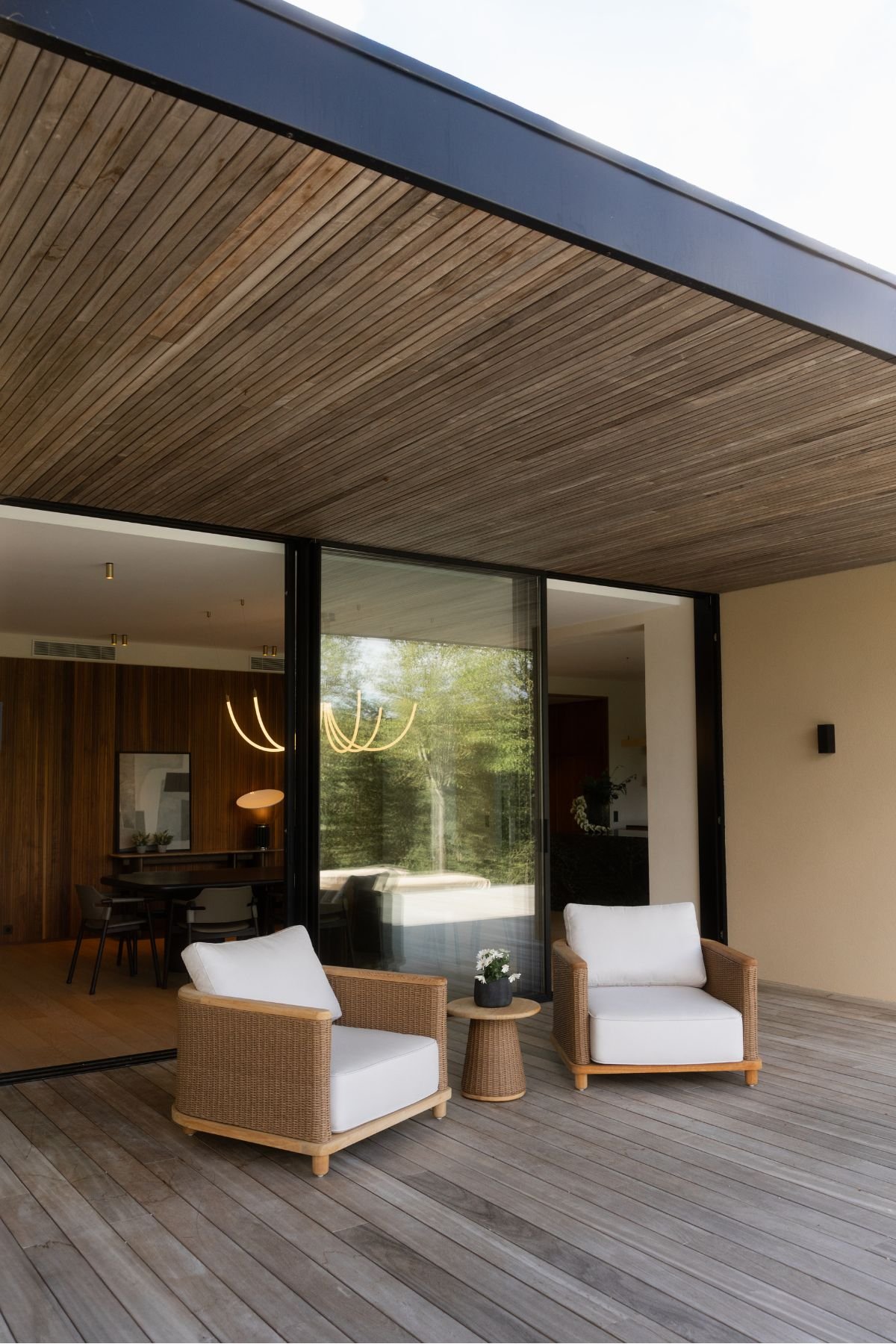 Zona exterior coberta com poltronas de exterior de jardim e mesa de apoio no terraço em deck de madeira.