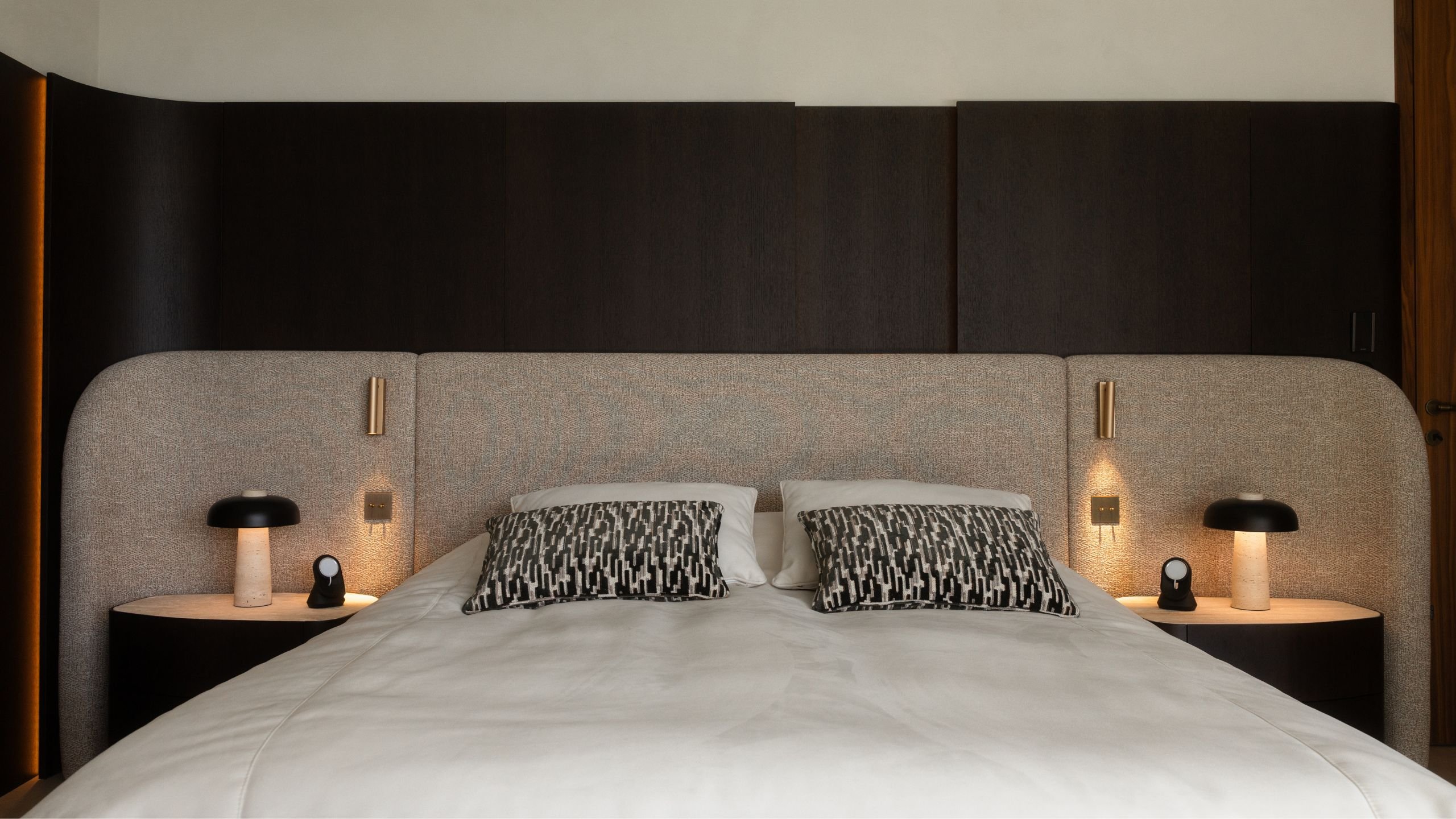 Cama de casal com cabeceira estofada curva de grande dimensão e mesas de cabeceira integradas.