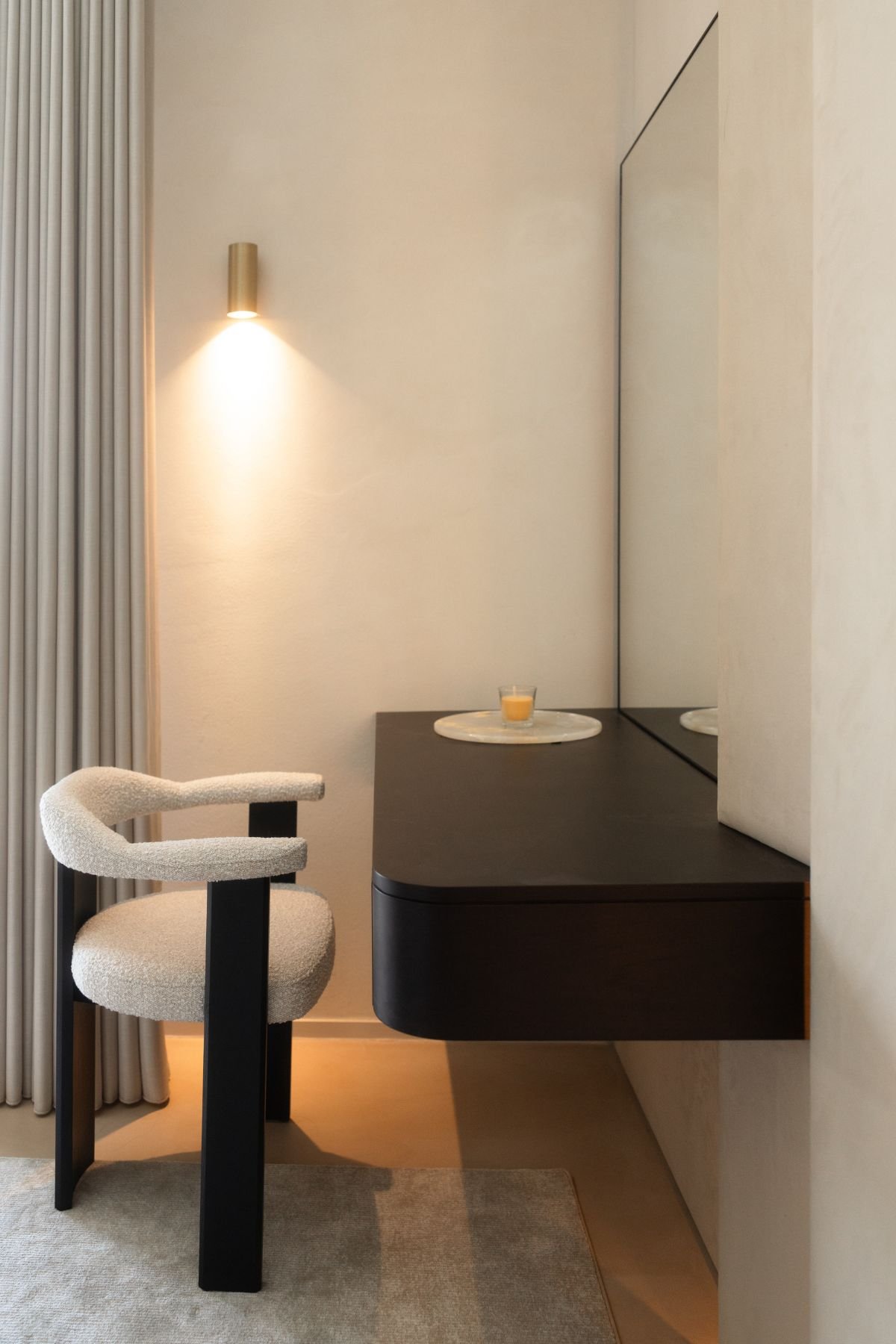 Cantinho de toucador suspenso com cadeira de quarto estofada em tecido boucle e iluminação indireta.