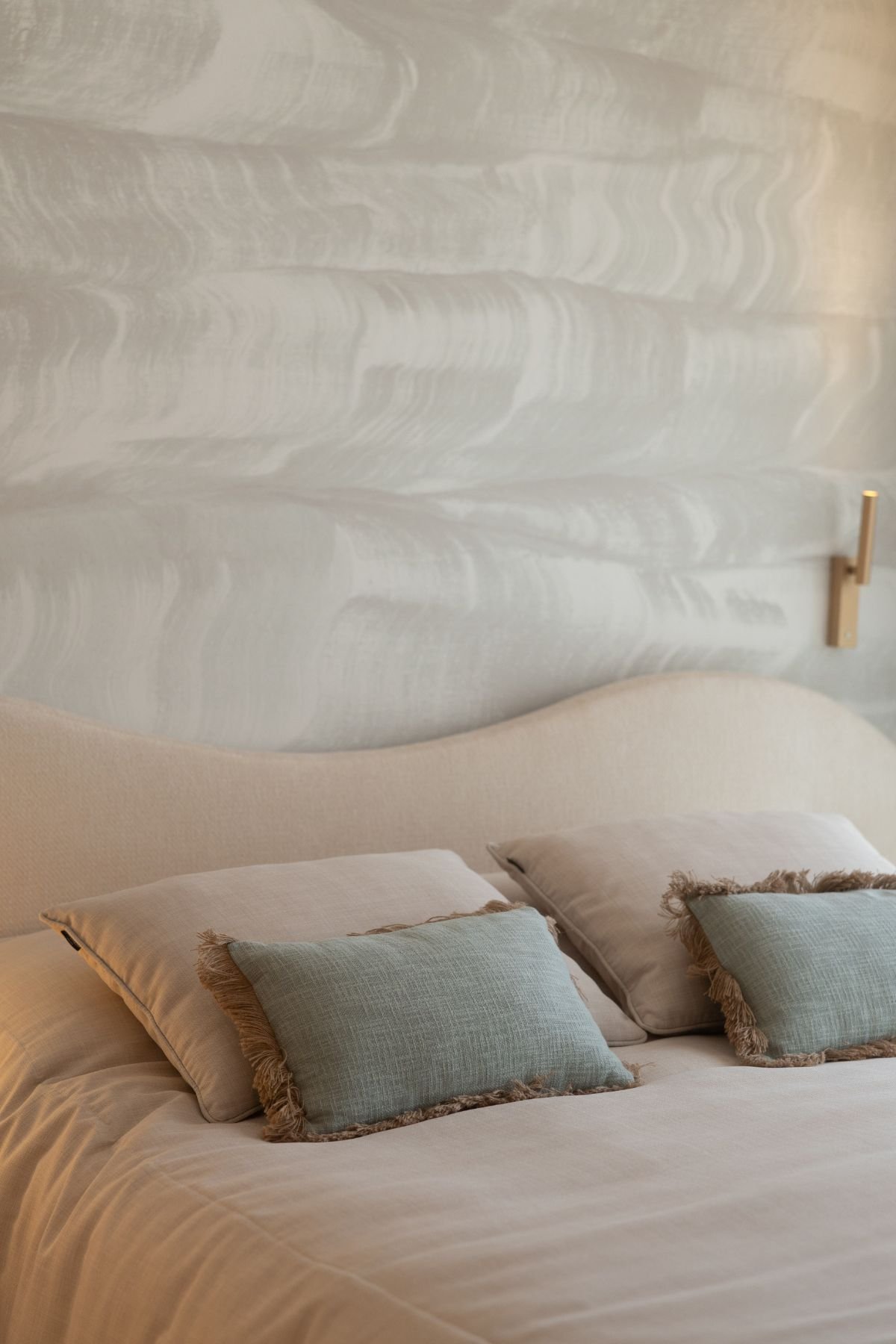 Pormenor da decoração de quarto infantil com almofadas de tom verde-água sobre a cama de casal e papel de parede textualizado.