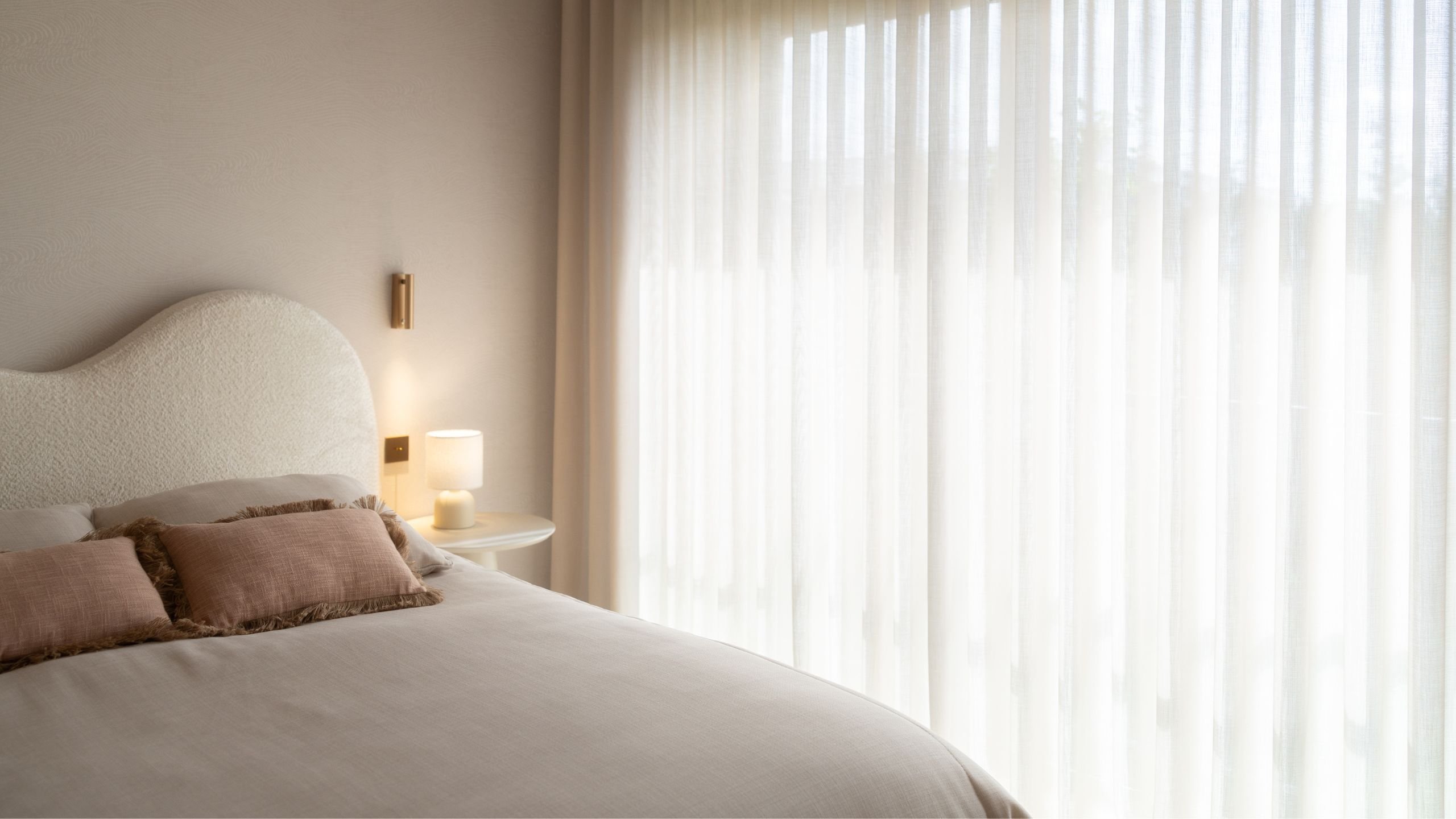 Cama no quarto infantil iluminada pela luz natural vinda da grande janela com cortinados leves.