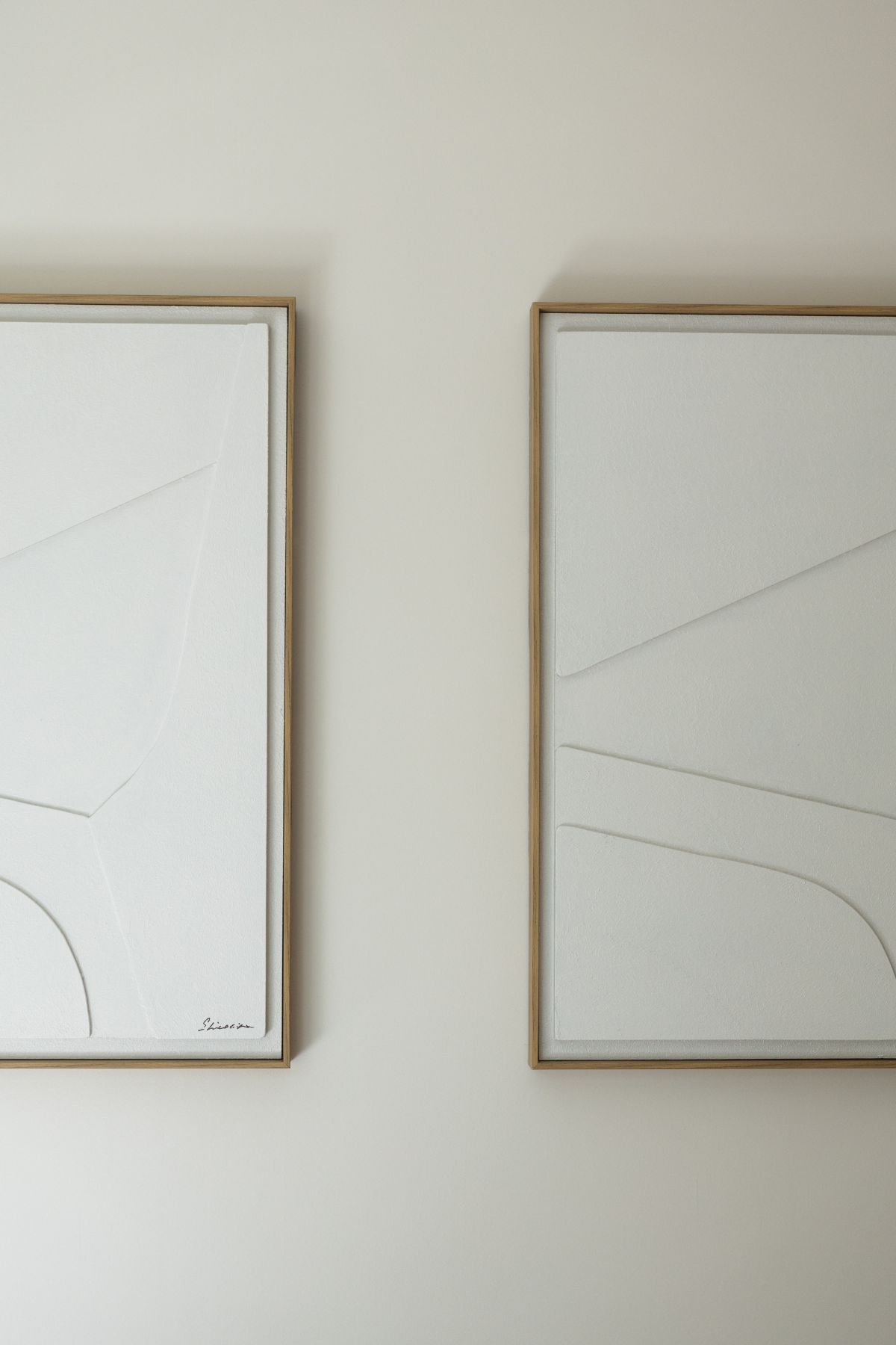 Dois quadros com arte em relevo branco e molduras de madeira minimalistas pendurados na parede.