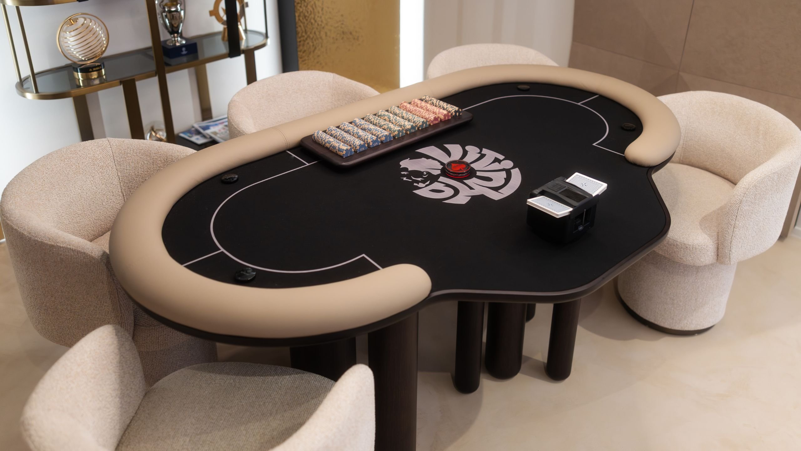 Vista superior da mesa de poker em madeira com bordo estofado em pele clara, fichas de jogo e cadeiras de jantar estofadas.