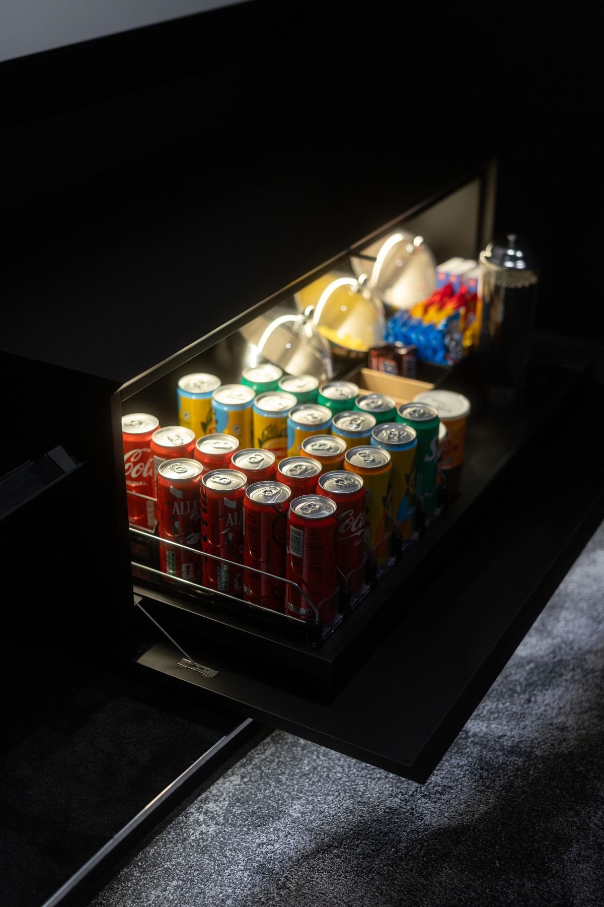 Pormenor do bar embutido com iluminação interior em LED, repleto de latas de bebidas e snacks para o cinema em casa.