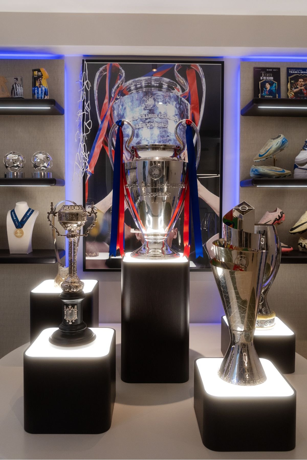 Plintos iluminados com troféus de futebol, incluindo o troféu da Liga dos Campeões da UEFA em destaque, em casas de luxo.