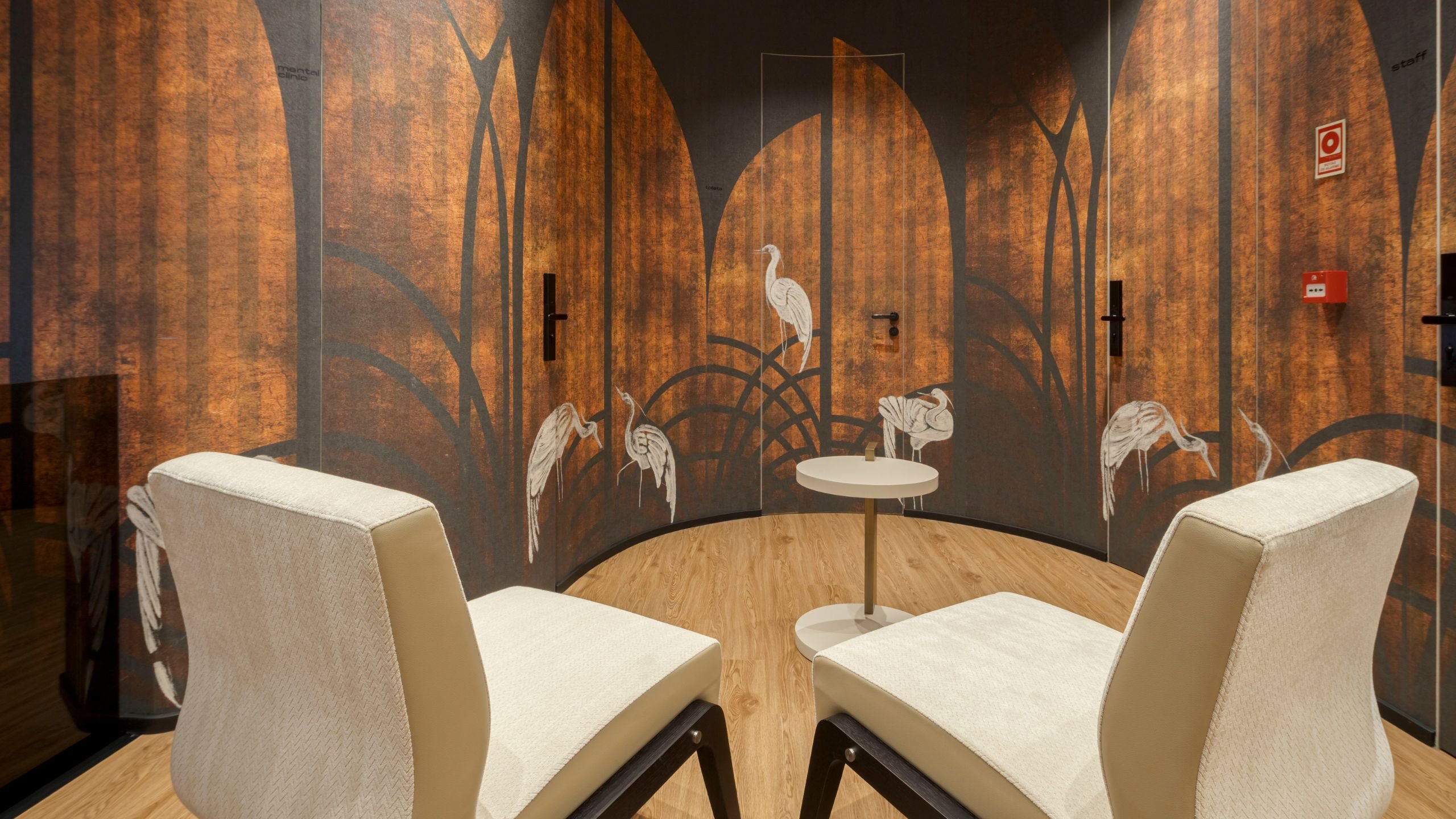 Vista ampla do hall de entrada do hotel com dois cadeirões, mesa de apoio e painel decorativo em tons dourados e pretos.