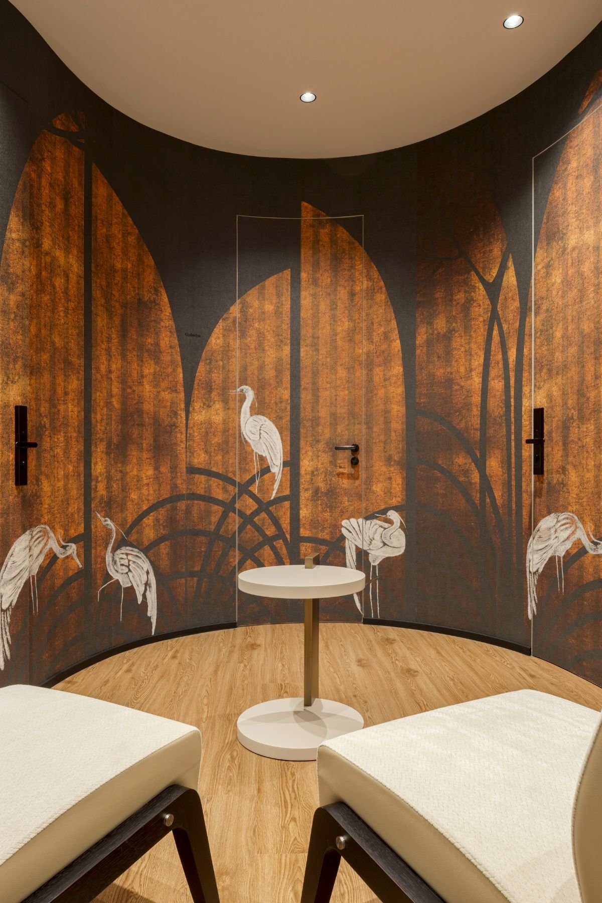 Hall de entrada com parede curva revestida a papel de parede com ilustrações de cegonhas, cadeirões Grace e mesa de apoio Club.