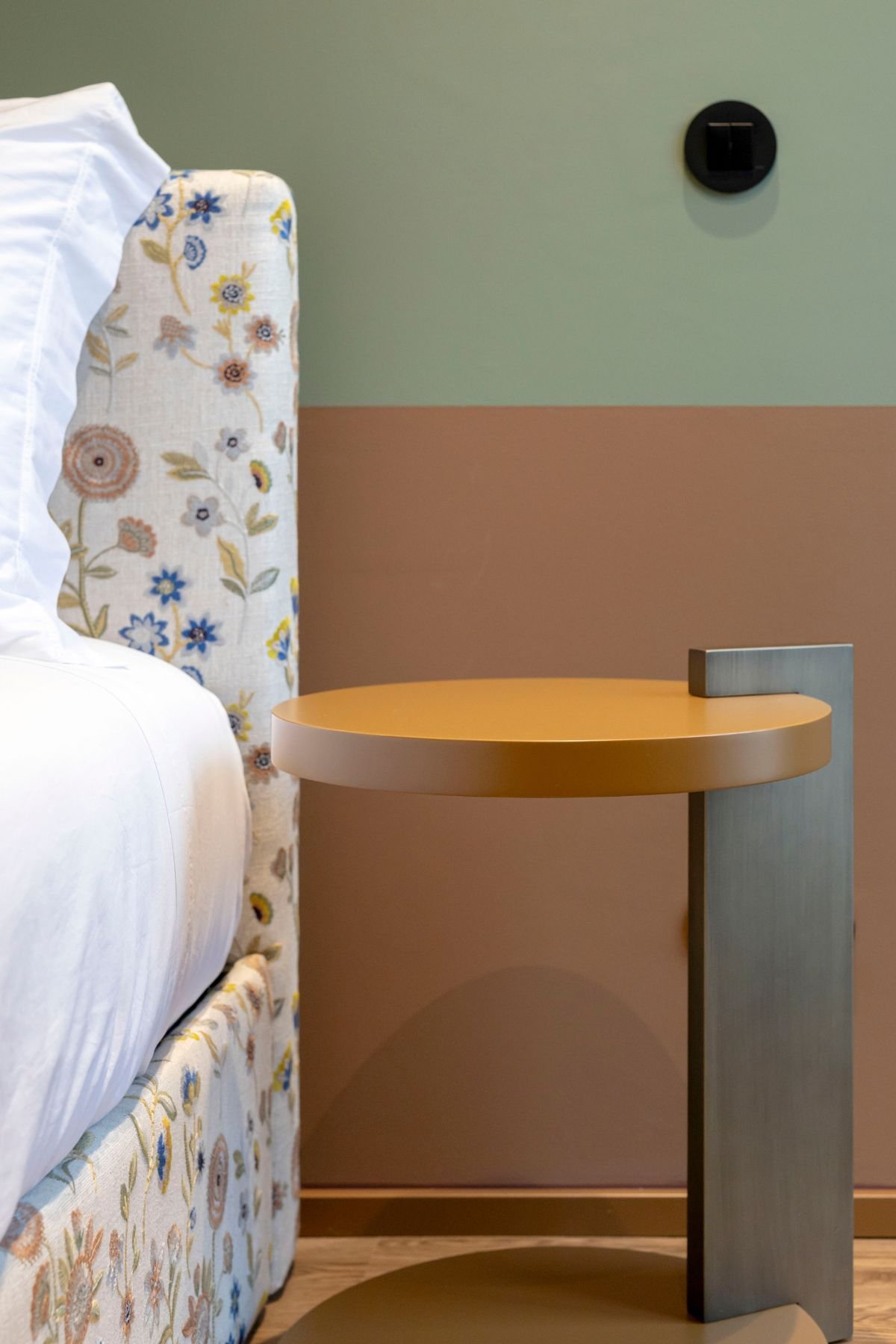Pormenor da mesa de apoio em lacado mate junto à cama com estofamento em tecido floral.