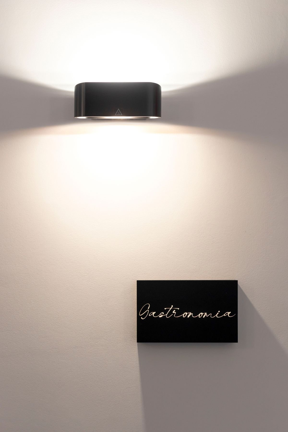 Aplique de parede iluminando a placa identificadora em tom escuro com a inscrição 