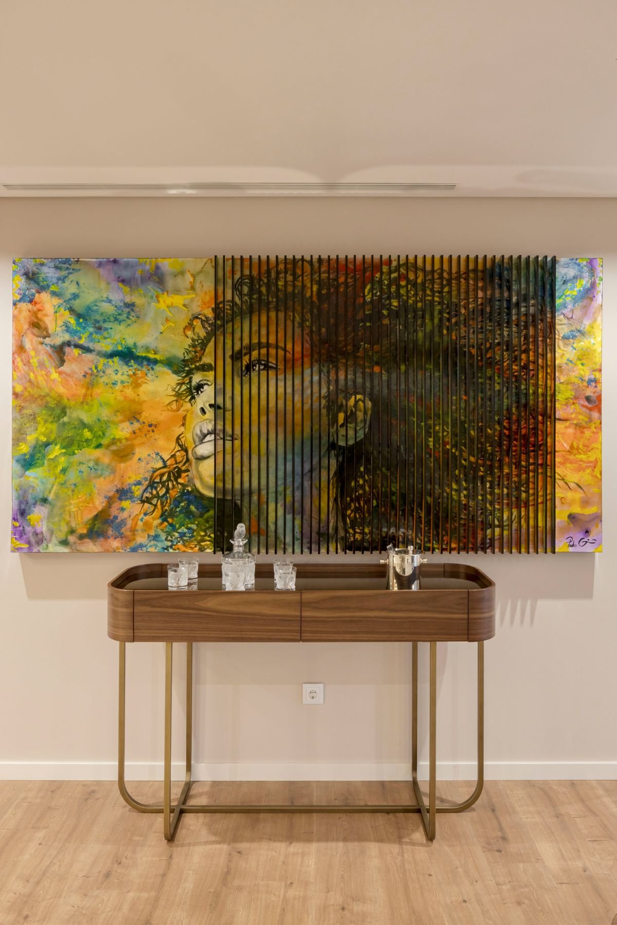 Consola His em madeira nogueira com garrafas decorativas sob quadro colorido do artista Pedro Guimarães.