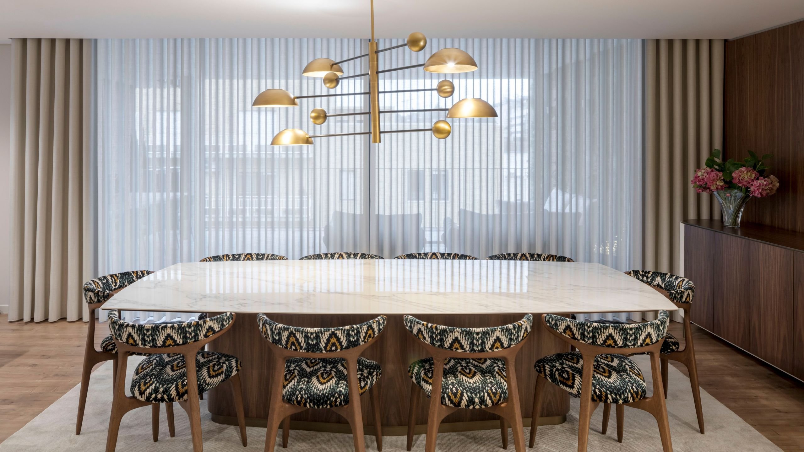 Sala de jantar com mesa de tampo cerâmico imitação mármore, cadeiras Bevel étnicas e candeeiro de teto dourado.