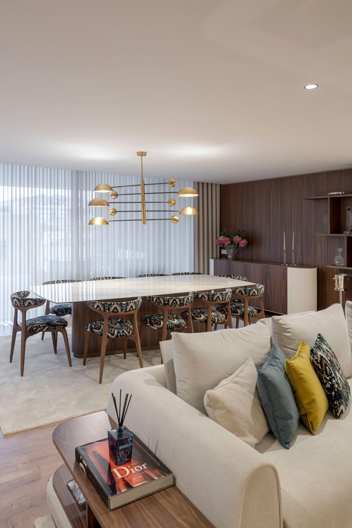 Transição entre o sofá claro da sala de estar e a zona de refeições com mesa Elea e aparador Club.