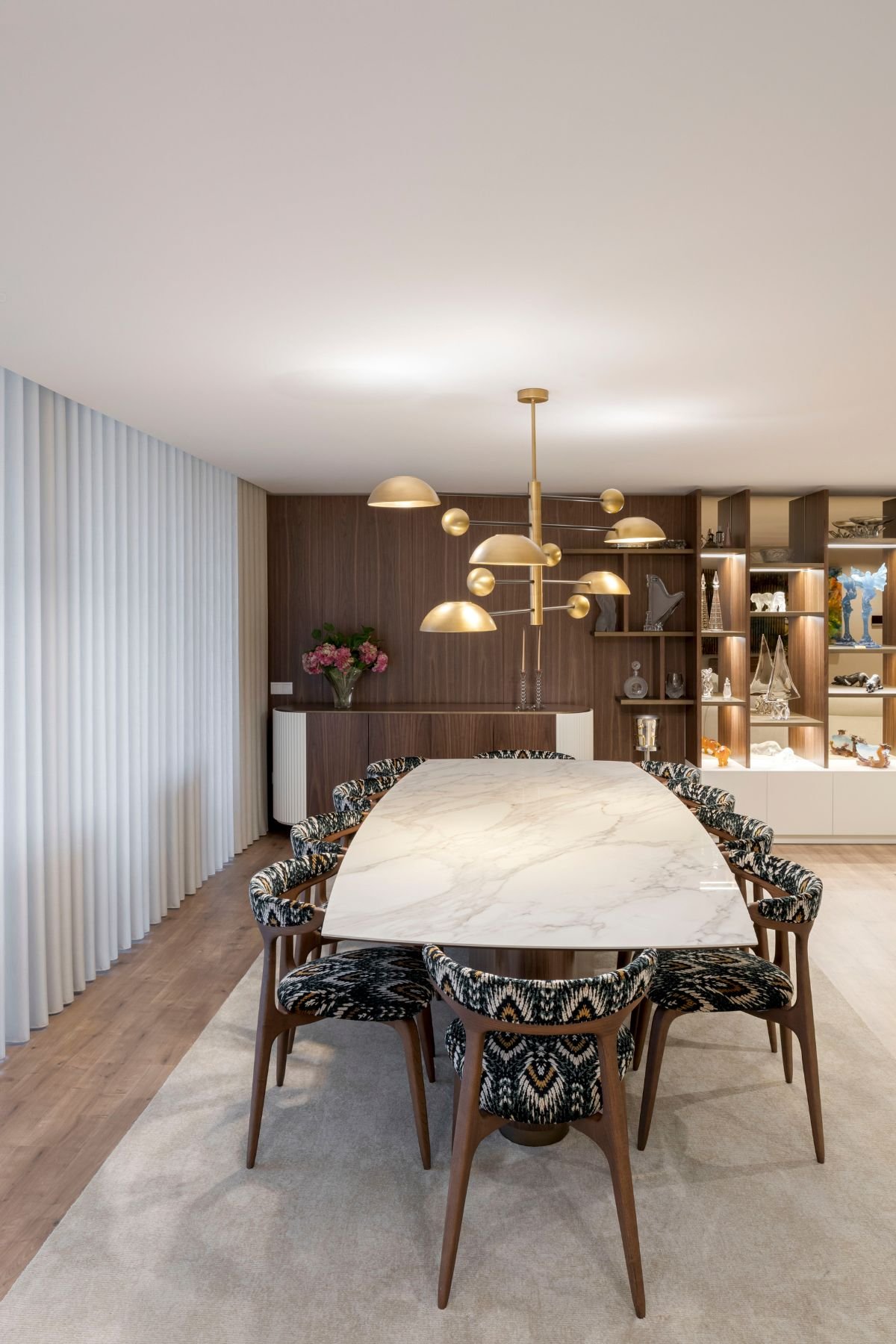 Vista frontal da mesa de jantar Elea com tampo cerâmico, cadeiras Bevel em tecido étnico e candeeiro suspenso dourado.