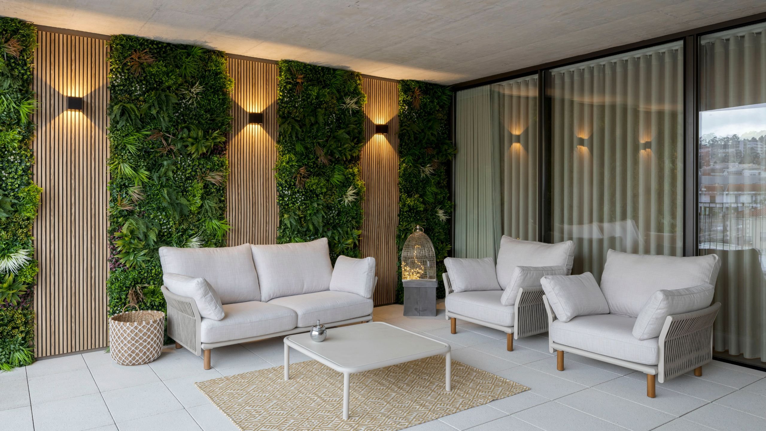 Área de lounge exterior com sofá, poltronas, mesa de centro, tapete e parede com painéis ripados e jardim vertical iluminado.