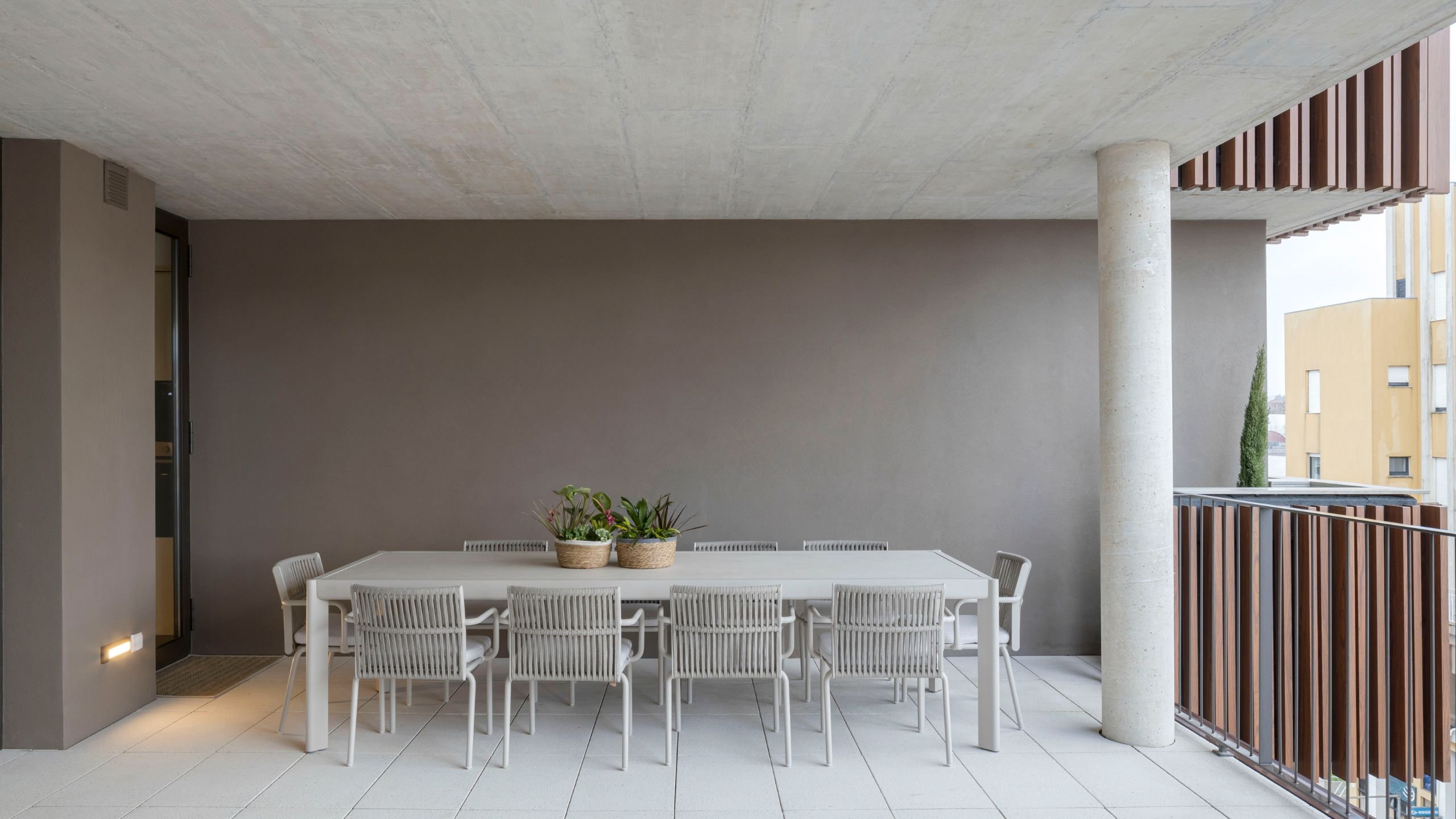 Vista ampla da zona de refeições exterior com mesa para dez pessoas na varanda coberta.