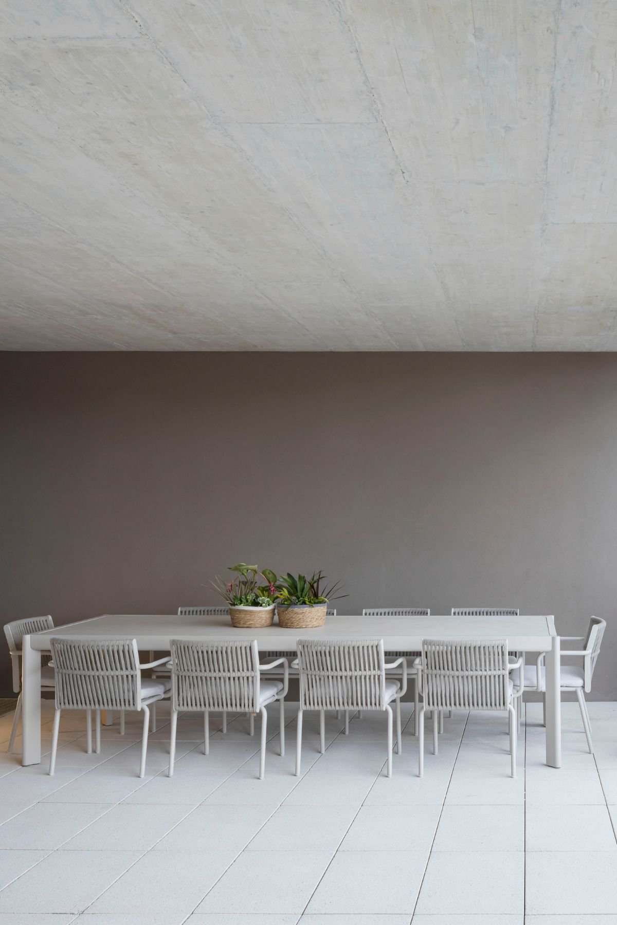 Conjunto de refeições de exterior composto por mesa longa clara e cadeiras trançadas na varanda.